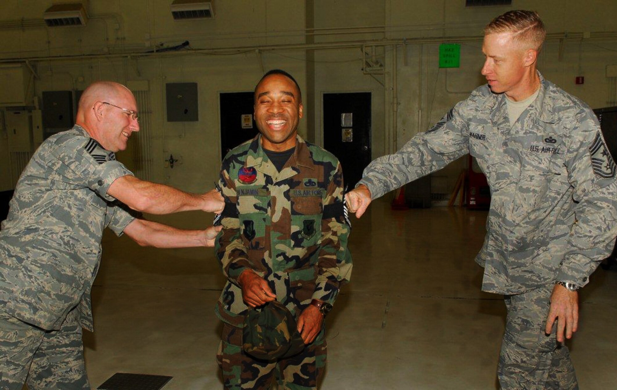 Senior Master Sgt. Peter Benjamin, 18th Component Maintenance Squadron, accepts the 'pain' of promotion as Chief Master Sgt. Bradley Korte, 18th CMS, and 18th Wing Command Chief Master Sgt. Michael Warner tack on chief stripes during a surprise visit Nov. 6. Sergeant Benjamin was among a dozen senior master sergeants selected for promotion to the Air Force's top enlisted rank after the Air Force Personnel Center released the chief master sergeant promotion list early Friday morning. (Air Force/Airman 1st Class Chad Warren)
