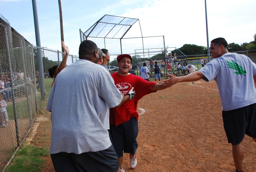 Jason Almadovar (in red), part of the “Armament” softball team , leading the team as both pitcher and slugger, is greeted at home after slamming a home run during
the softball tournament as part of October's wing picnic. (U.S. Air Force photo/TSgt Shawn David McCowan)
