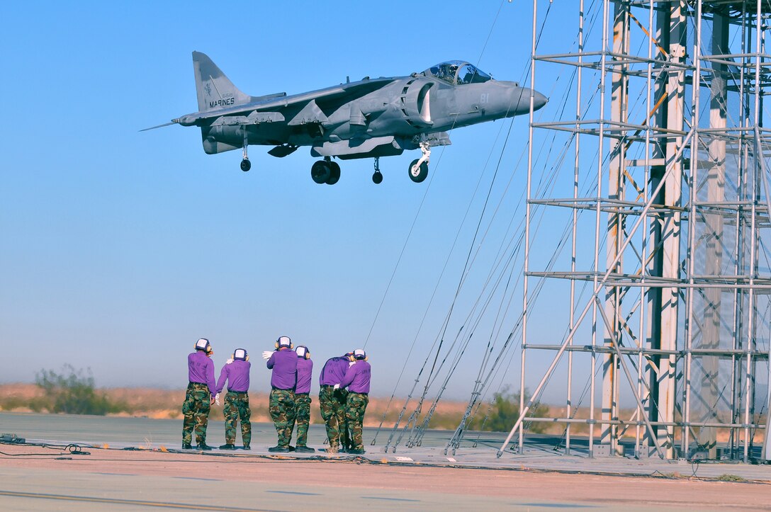 Navy aviation fuel technicians from the USS Green Bay watch as Maj. Bill Rothermel, AV-8B Harrier test pilot with Air Test and Evaluation Squadron 31, lands vertically on Auxiliary Airfield 2 in Yuma, Ariz., Nov. 5, 2009. The squadron and the USS Green Bay flight deck crew practiced working together at the airfield, which simulates the deck of a ship, to prepare for their upcoming testing period aboard the Green Bay. The Green Bay, commissioned January 2009, is part of the Navy’s new class of amphibious transport dock ship built specifically for helicopter operations. The squadron tested Harrier operations aboard the ship Nov. 11-15, 2009, to ensure that its design doesn’t inhibit use by Harriers in case of emergencies. Since the Green Bay is intended for helicopter use, many of its flight crew are inexperienced working with Harriers.  “A lot of our crew members are very new to the fleet and many have never worked with jets before,” said Petty Officer 1st Class Albaro Rodriguez, USS Green Bay aviation fuel technician. “This is giving them a good chance to get prepared for possible emergency situations.”