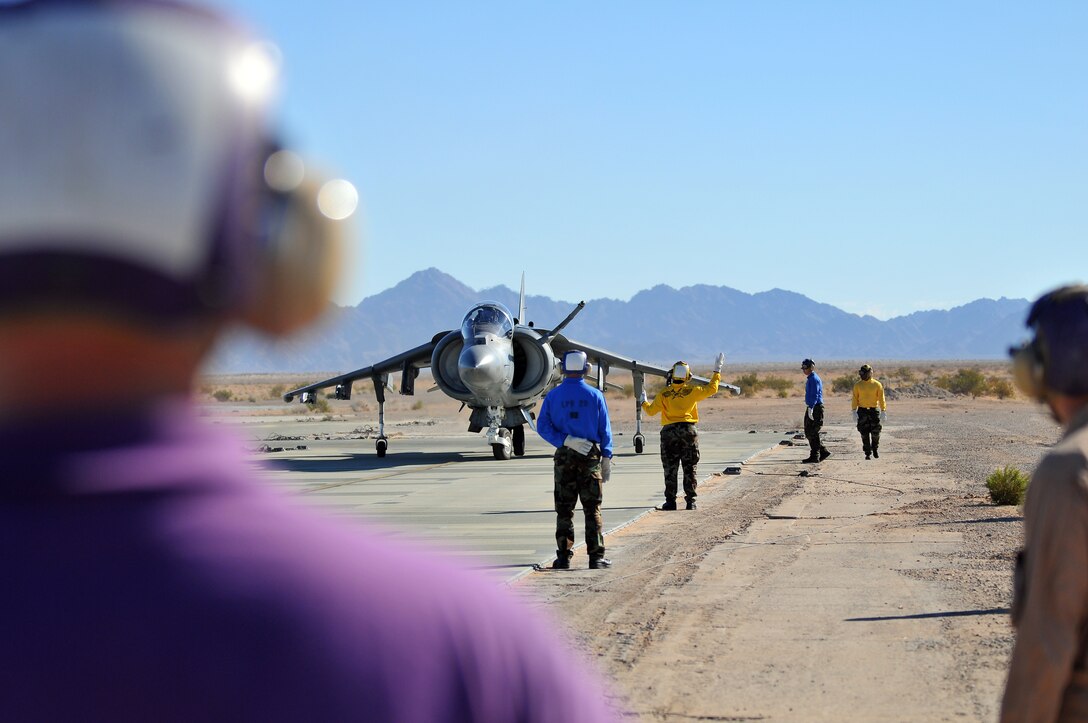 Navy flight deck crewmen from the USS Green Bay observe as Maj. Bill Rothermel, AV-8B Harrier test pilot with Air Test and Evaluation Squadron 31, taxis to be refueled at Auxiliary Airfield 2 in Yuma, Ariz., Nov. 5, 2009. The squadron and the USS Green Bay flight deck crew practiced working together at the airfield, which simulates the deck of a ship, to prepare for their upcoming testing period aboard the Green Bay. The Green Bay, commissioned January 2009, is part of the Navy’s new class of amphibious transport dock ship built specifically for helicopter operations. The squadron tested Harrier operations aboard the ship Nov. 11-15, 2009, to ensure that its design doesn’t inhibit use by Harriers in case of emergencies. Since the Green Bay is intended for helicopter use, many of its flight crew are inexperienced working with Harriers.  “A lot of our crew members are very new to the fleet and many have never worked with jets before,” said Petty Officer 1st Class Albaro Rodriguez, USS Green Bay aviation fuel technician. “This is giving them a good chance to get prepared for possible emergency situations.”