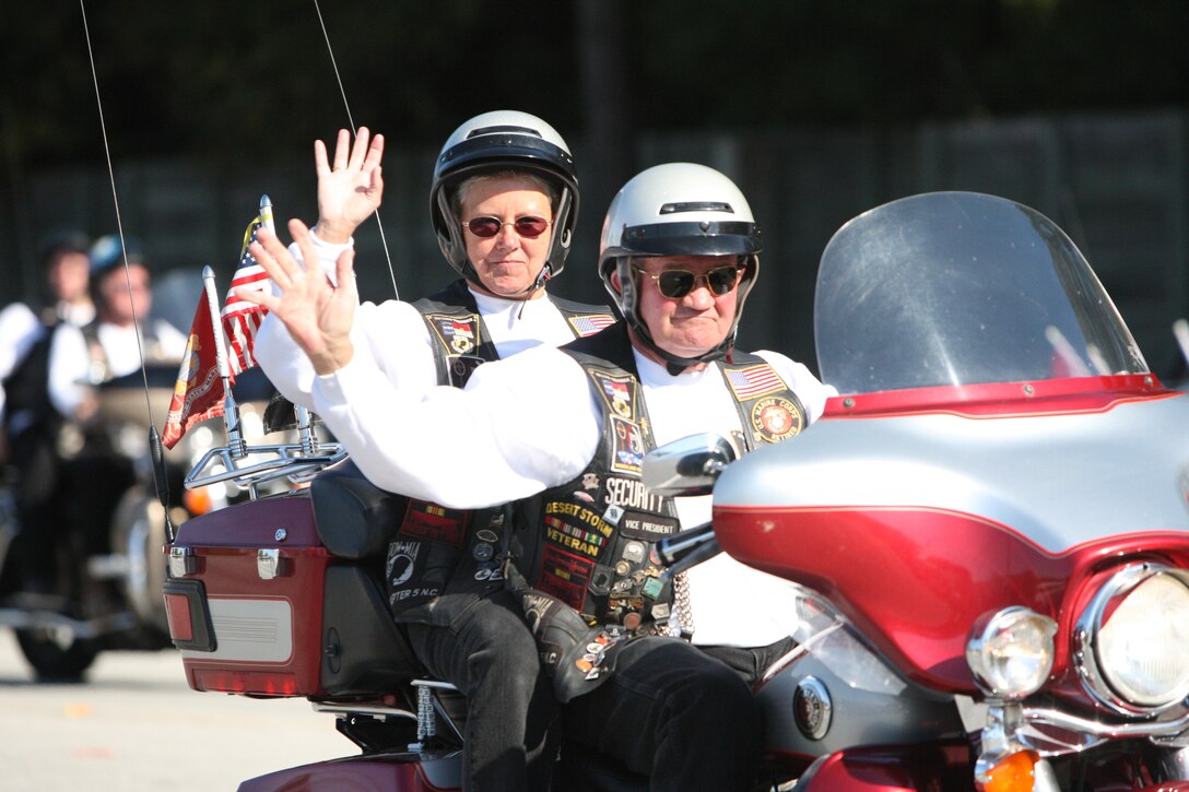 Two members of the Rolling Thunber bike club wave at the crowd as they drive by in the Veterans Day Parade in Jacksonville, N.C., Nov. 6. The bike was decorated in American and Marine Corps flags.