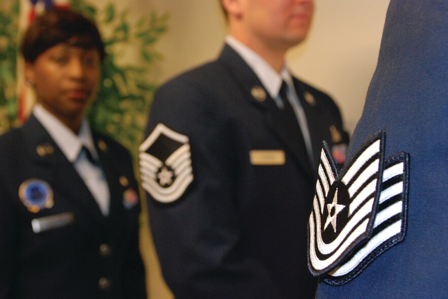 Tech. Sgt. Vincent Johnson’s new Technical Sergeant rank is fastened to his old Staff Sergeant rank with a loop of duct tape. He was promoted in a ceremony Oct. 30. Master Sgt. Kamala Thigpen (left) and Master Karl Perron were promoted and inducted as senior non-commissioned officers during the same ceremony. (U.S. Air Force photo by Megan Just)