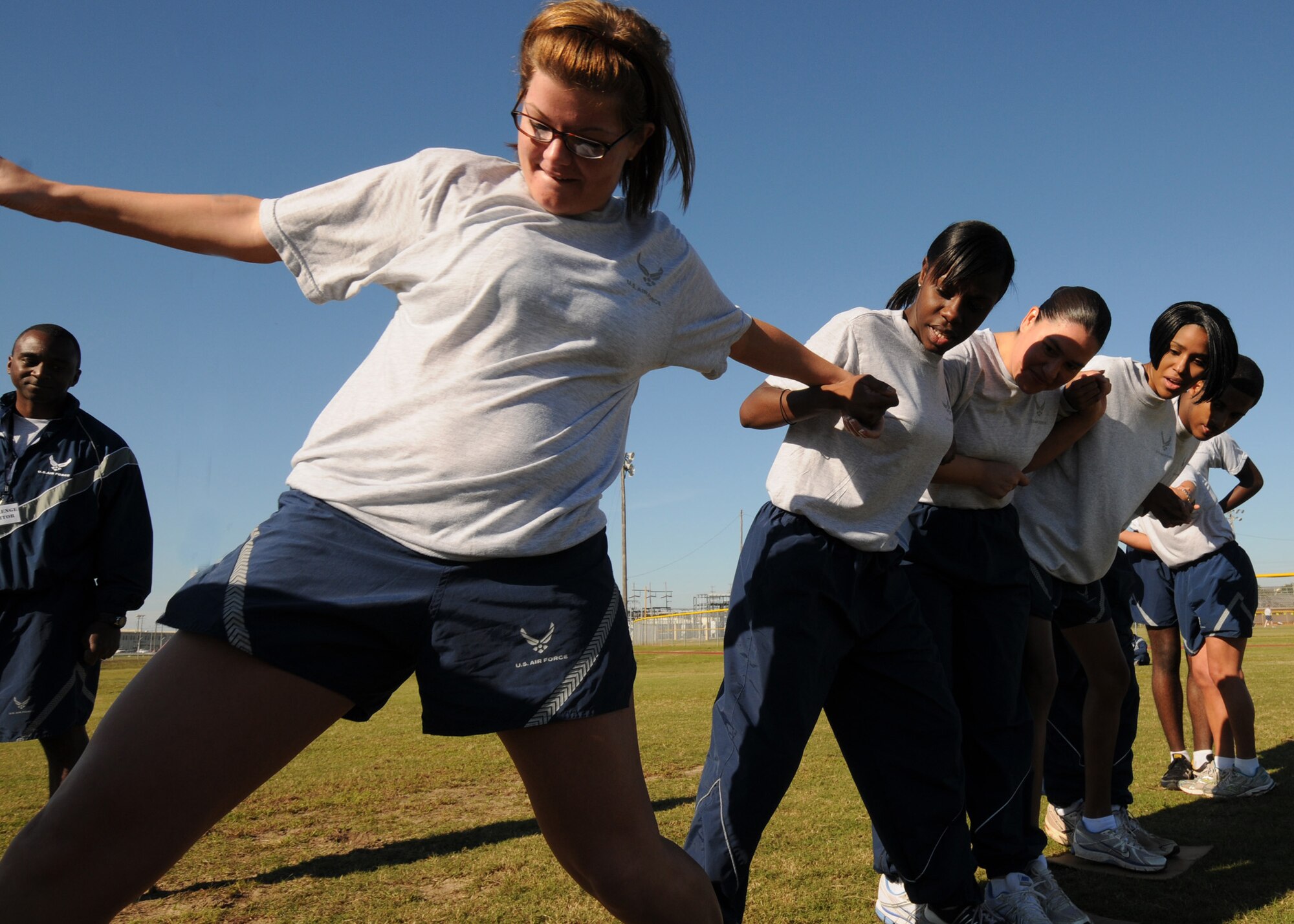Team members help an Airman balance as she reaches for the next card board square during a teamwork activity at the Eglin Wingman Day Nov. 5.  Teams had to move from one side of the field to the other by walking on cardboard squares.  Teams came up with varying game plans to get their members to the other side without taking their feet off the cardboard.  (Air Force photo/Samuel King Jr.)
