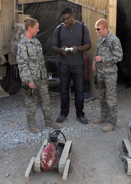 Michael Strahan, an announcer with "Fox NFL Sunday," learns to operate an explosive ordnance disposal robot at Bagram Airfield, Afghanistan, Nov. 6, 2009. Staff Sgt. Elizabeth Spradley (left) and Senior Airman James Dobrynski, both EOD technicians with the 755th Air Expeditionary Group, had Mr. Strahan practice picking up an autographed NFL football. Sergeant Spradley is deployed from Spangdahlem Air Base, Germany. Airman Dobrynski is deployed from Luke Air Force Base, Ariz. The Fox NFL team is scheduled to broadcast live from here Nov. 8. The team of Curt Menefee, Terry Bradshaw, Howie Long, Michael Strahan, Jimmy Johnson and Jay Glazer will do the special just three days before Veterans Day. (U.S. Air Force photo/Senior Airman Felicia Juenke) 
