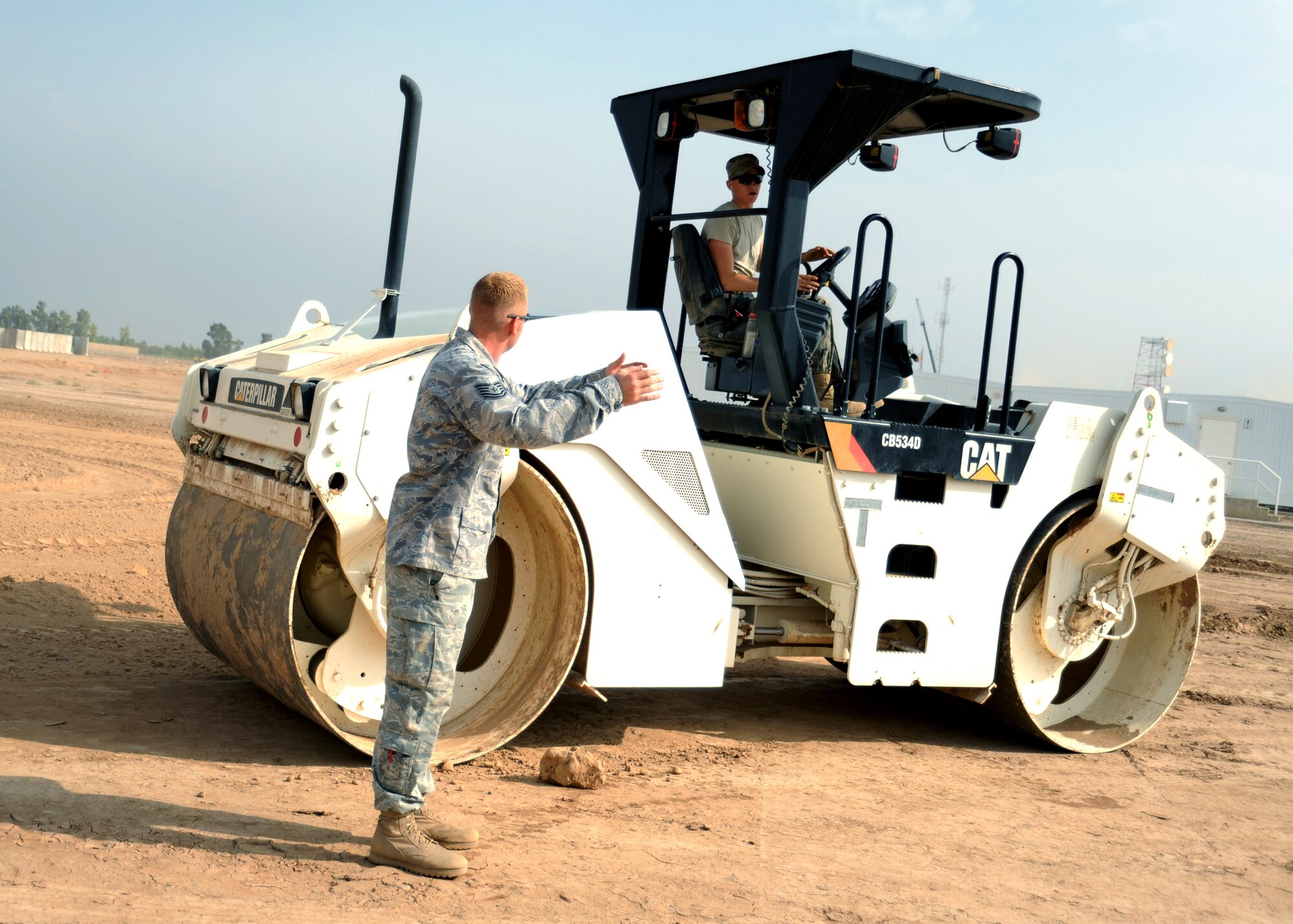 JOINT BASE BALAD, Iraq -- Tech. Sgt. Orlin Rohde, 732nd Expeditionary Civil Engineer Squadron heavy equipment operator and project manager, directs Airman Marshall Hess as he drives a vibratory roller to prepare the grounds for a new container repair yard Nov. 2, 2009. By using containers repaired here instead of purchasing new ones, the projected savings total more than $100 million as military assets withdraw from Iraq. (U.S. Air Force photo/Senior Airman Christopher Hubenthal)