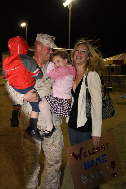 MARINE CORPS AIR GROUND COMBAT CENTER TWENTYNINE PALMS, Calif. -Chief Warrant Officer 2 Chris Kamm, a chemical, biological, radiological, nuclear defense officer with Headquarters Battery, 3rd Battalion, 11th Marine Regiment, holds his two children as his wife stands beside him at 3rd Bn., 11th Marines parking lot Saturday. Some of the families brought signs children made to welcome home their fathers. (U.S. Marine Corps photo by Lance Cpl. Andrew D. Thorburn)
