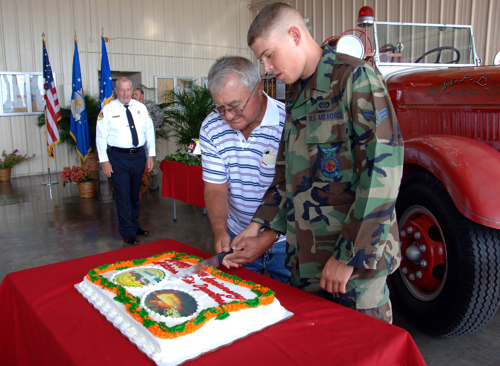 HICKAM AIR FORCE BASE, Hawaii -- Retired Chief Clifford Faria and Airman 1st Class Christopher Conro, 15th Civil Engineer Squadron firefighter, perform the cake cutting Nov 6.  The two represent the oldest and the youngest firefighters present during the 70th Anniversary Ceremony of the Hickam Fire Department's establishment at Hickam Air Force Base.  (U.S. Air Force photo/Vanessa M. Forloine)