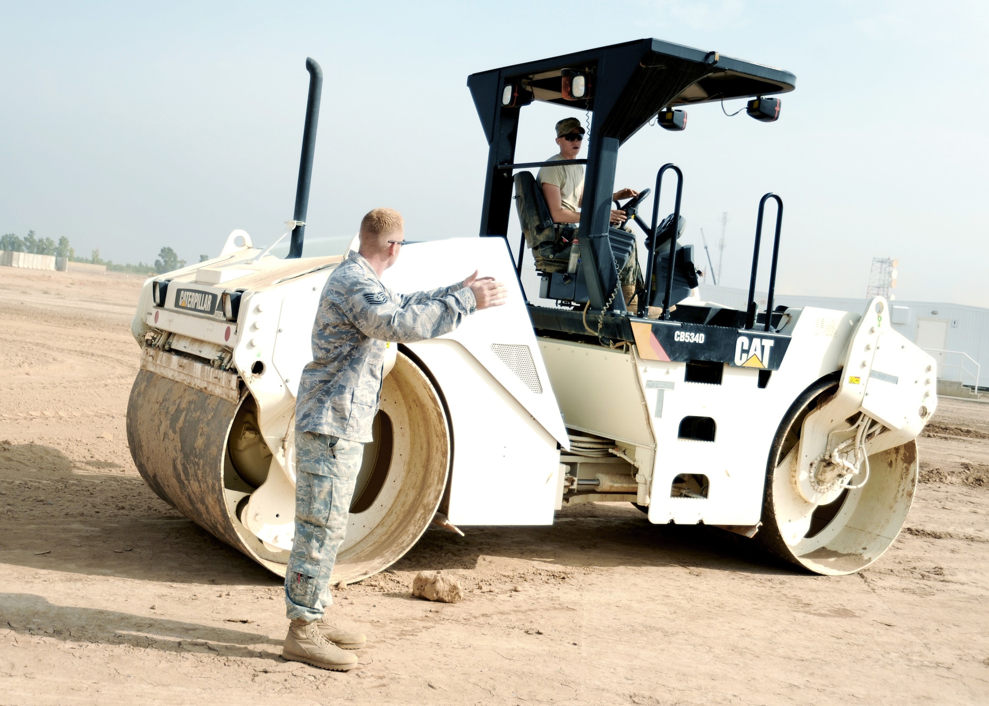 JOINT BASE BALAD, Iraq -- Tech. Sgt. Orlin Rohde, 732nd Expeditionary Civil Engineer Squadron heavy equipment operator and project manager, directs Airman Marshall Hess as he drives a vibratory roller to prepare the grounds for a new container repair yard Nov. 2, 2009. By using containers repaired here instead of purchasing new ones, the projected savings total more than $100 million as military assets withdraw from Iraq. (U.S. Air Force photo/Senior Airman Christopher Hubenthal) 