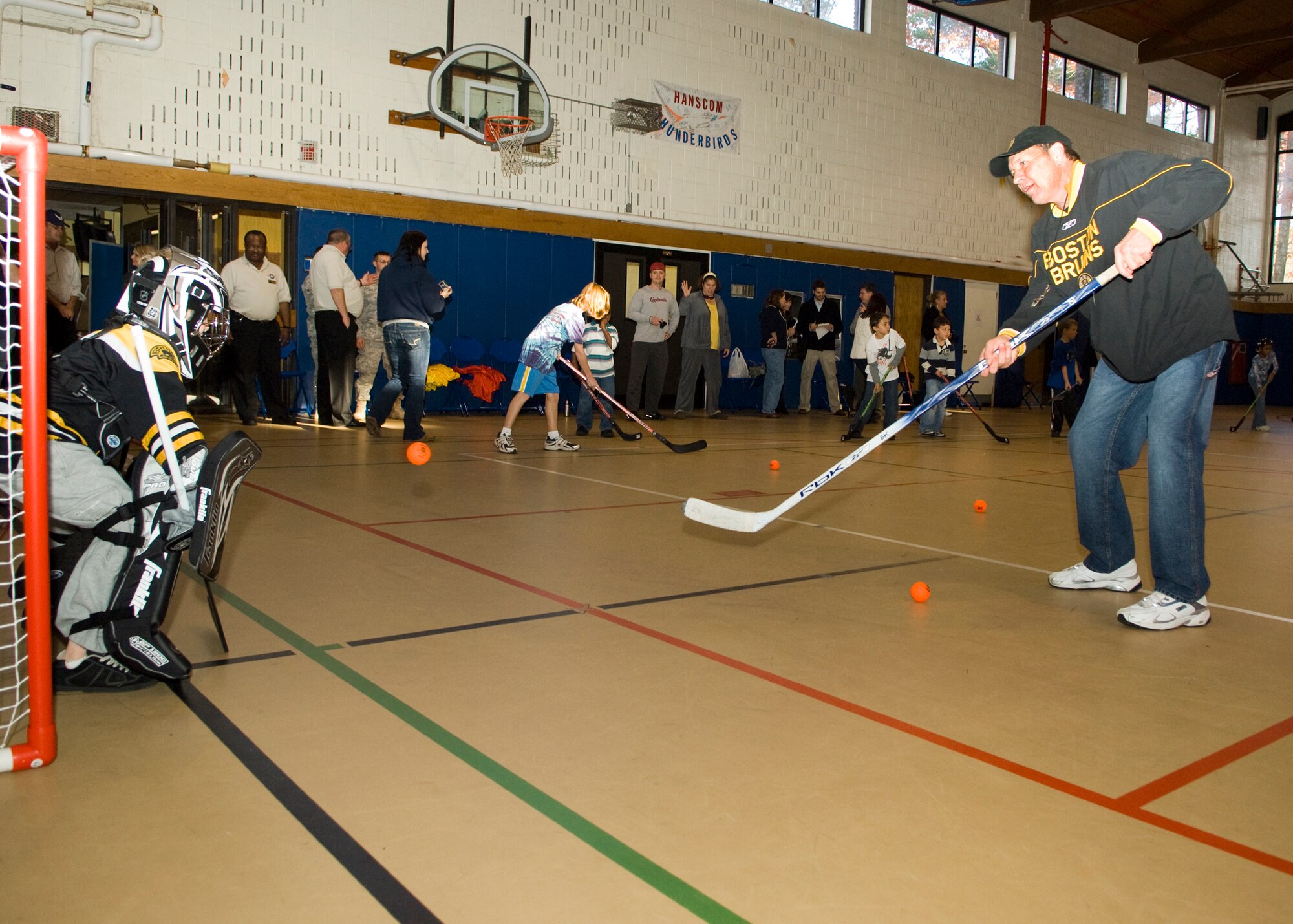HANSCOM AIR FORCE BASE, Mass. – Boston Bruins alumnus Tommy Songin takes a shot on goalie Justin Netemeyer during an Air Force Family Week street hockey event at the Hanscom Youth Center, Nov. 4, sponsored by the Boston Bruins and Operation Homefront. Bruins staff led Hanscom children through a number of street hockey drills focusing on the fundamentals of play. The Bruins donated all of the street hockey equipment they brought to the base to Hanscom’s Youth Center so children could continue to enjoy the game. (U.S. Air Force photo by Walter Santos)