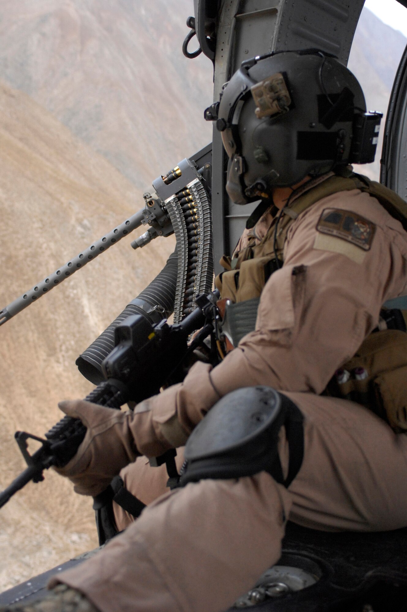 Staff Sgt. Justin Schramm, an aerial gunner for an HH-60G Pave Hawk sits behind his M2 .50 caliber machine gun during a flight. Sergeant Schramm is deployed with the 33rd Expeditionary Rescue Squadron from Kadena Air Base, Japan, and his job is to protect servicemembers on the ground  providing aid to injured people. Originally from Eugene, Ore., Sergeant Schramm loves his job because it allows him handle "many kinds of cool gadgets." (U.S. Air Force photo/Senior Airman Susan Tracy) 