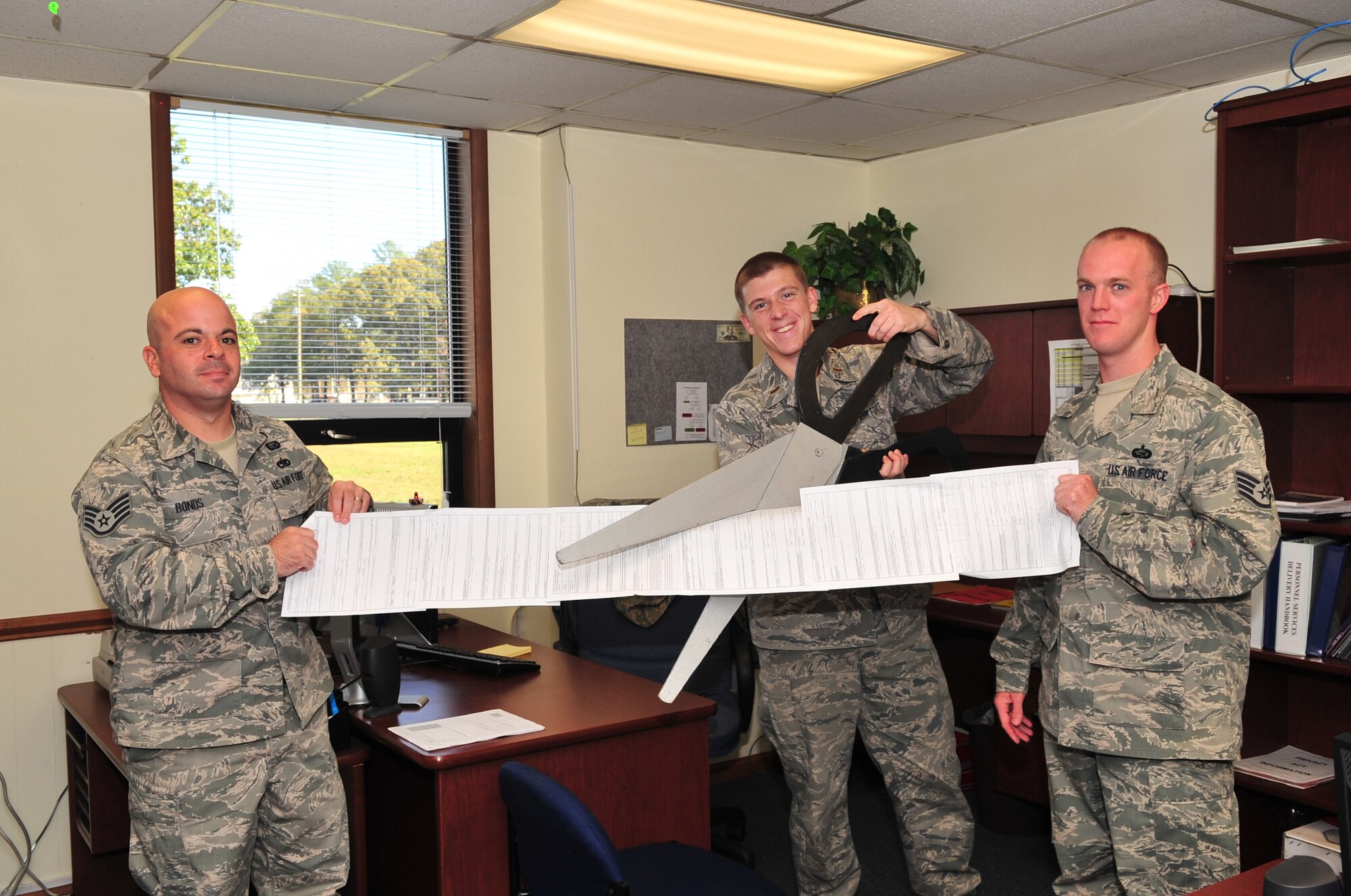 2nd Lt. Mark Honnen, 4th Force Support Squadron chief of force management operations, cuts a ribbon made of enlisted and officer performance reports held by Staff Sgts.  Shaun Bonds and William Guthery, 4th FSS force management operations supervisors, on Seymour Johnson Air Force Base, N.C., Nov. 6, 2009. The ribbon cutting symbolized the demise of a paper system while the Air Force's Evaluation Management System quickly becomes electronically based. (U.S. Air Force photo/Airman 1st Class Rae Perry) 
