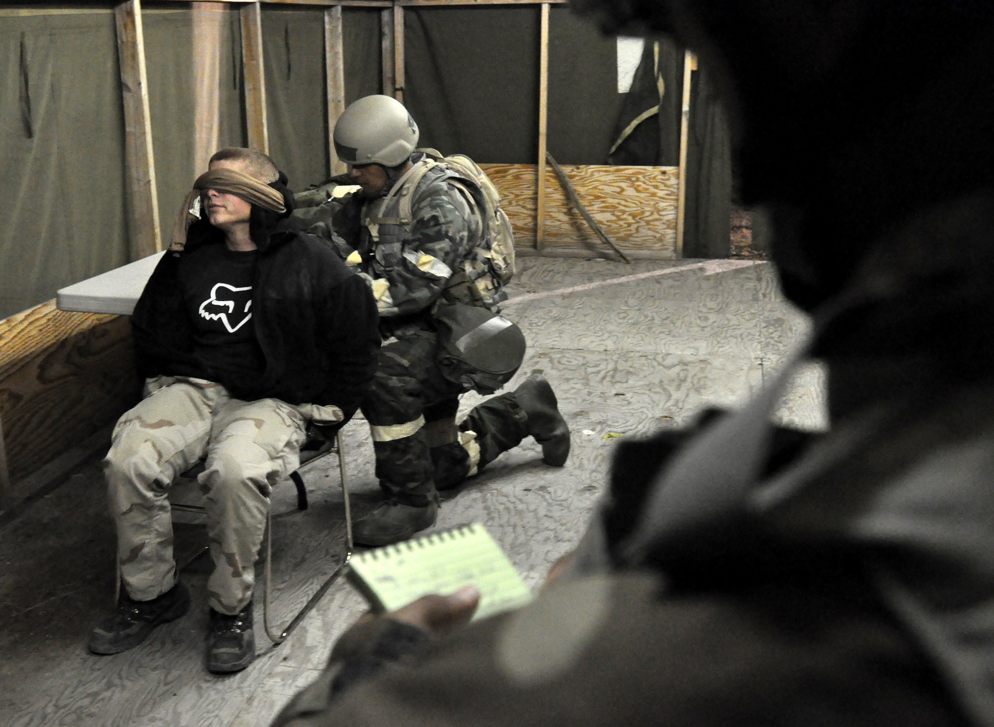 Senior Airman Brian Theobald, opposing forces team member, is interrogated by Senior Airman Nicholas Jack, while Tech. Sgt. Chris Field fills out identification tag for the captive. (U.S. Air Force photo/Staff Sgt. Kyle Brasier)