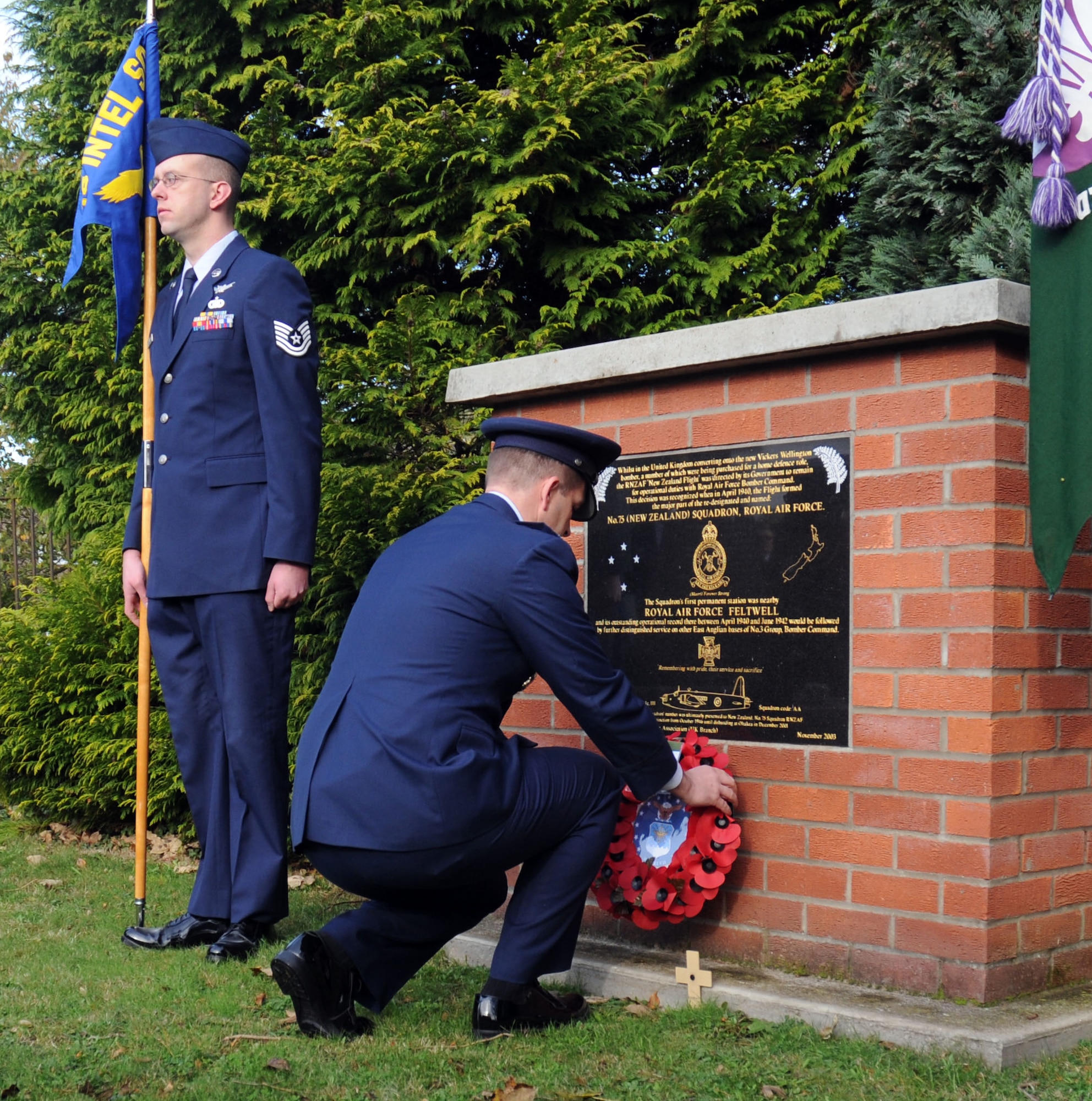 Lt. Col. Sean Murphy, 48th Communications Squadron commander, lays down a poppy wreath at the Feltwell War Memorial, as Tech. Sgt Robert Hotzfeld, 18th Intelligence Squadron Detachment 4 Space systems analyst, serves as guidon bearer during a Remembrance Sunday memorial service Nov. 8. In the U.K., wearing red poppies and laying poppy wreaths at memorial sites is a way to honor those who lost their lives or were injured during war. (U.S. Air Force photo by Staff Sgt. Megan Lyon)