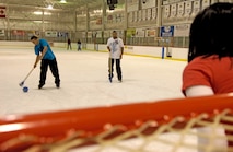 MINOT, N.D. -- Senior Airman Angelo Tapang, 91st Missile Wing client service administrator, takes a shot at the goal as his girlfriend, Megan Dougherty, guards the goal during a game of broom ball at the Maysa Arena Nov. 6 here. Their friend, Senior Airman Wesley Berry, 5th Communications Squadron knowledge operator, assisted Airman Tapang on the shot. The three friends came to skate as one of the activities the Airman and Family Readiness Center put together for Air Force Family Week. The purpose of the week’s events is to focus collective attention of AF leadership on its families and recognize their service. (U.S. Air Force photo by Airman 1st Class Benjamin Stratton)