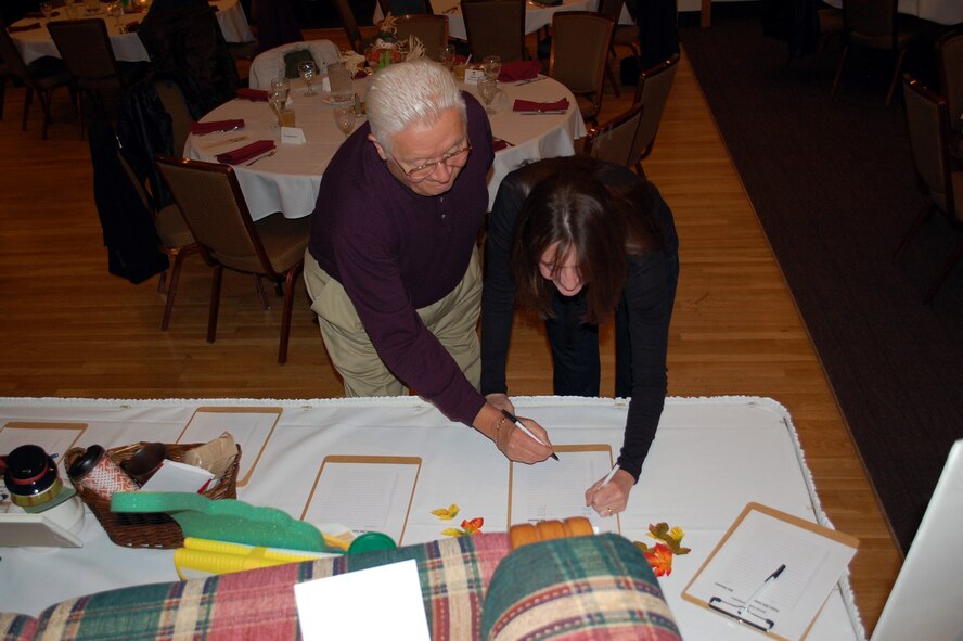 Retired Col. Steve Kubick and Karen Fortney make entries on a silent auction item up for bid at the Malmstrom Spouses' Club Mercantile Auction Nov. 7. (U.S. Air Force photo/Valerie Mullett)