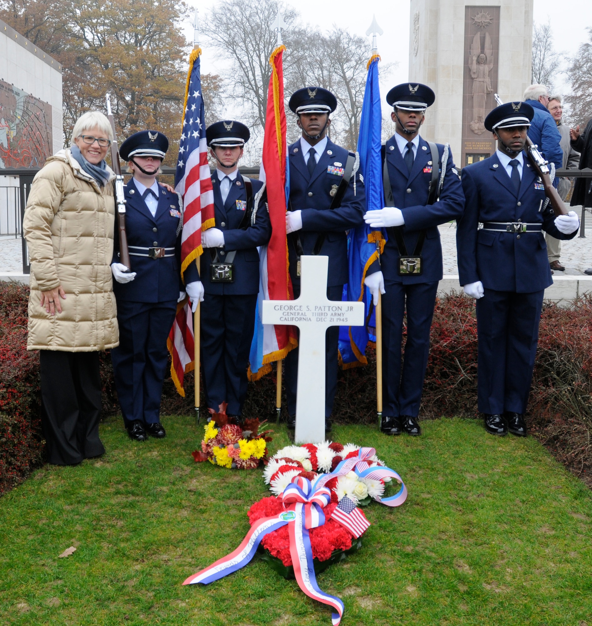 SPANGDAHLEM AIR BASE, Germany -- The 702nd Munitions Support Squadron Color Guard from Buechel Air Base, Germany, stands at attention in front of the grave of Gen. George S. Patton Jr., Third Army commander during World War II, with Helen Patton-Plusczyk, General Patton's granddaughter, during the annual Veterans Day ceremony at the Luxembourg American Cemetery and Memorial in Luxembourg City Nov. 11. The 50.5 acre cemetery, which is one of 14 American cemeteries established overseas after World War II, contains the remains of more than 5,000 American servicemembers who died during World War II. (U.S. Air Force photo/Maj. Jillian Torango)