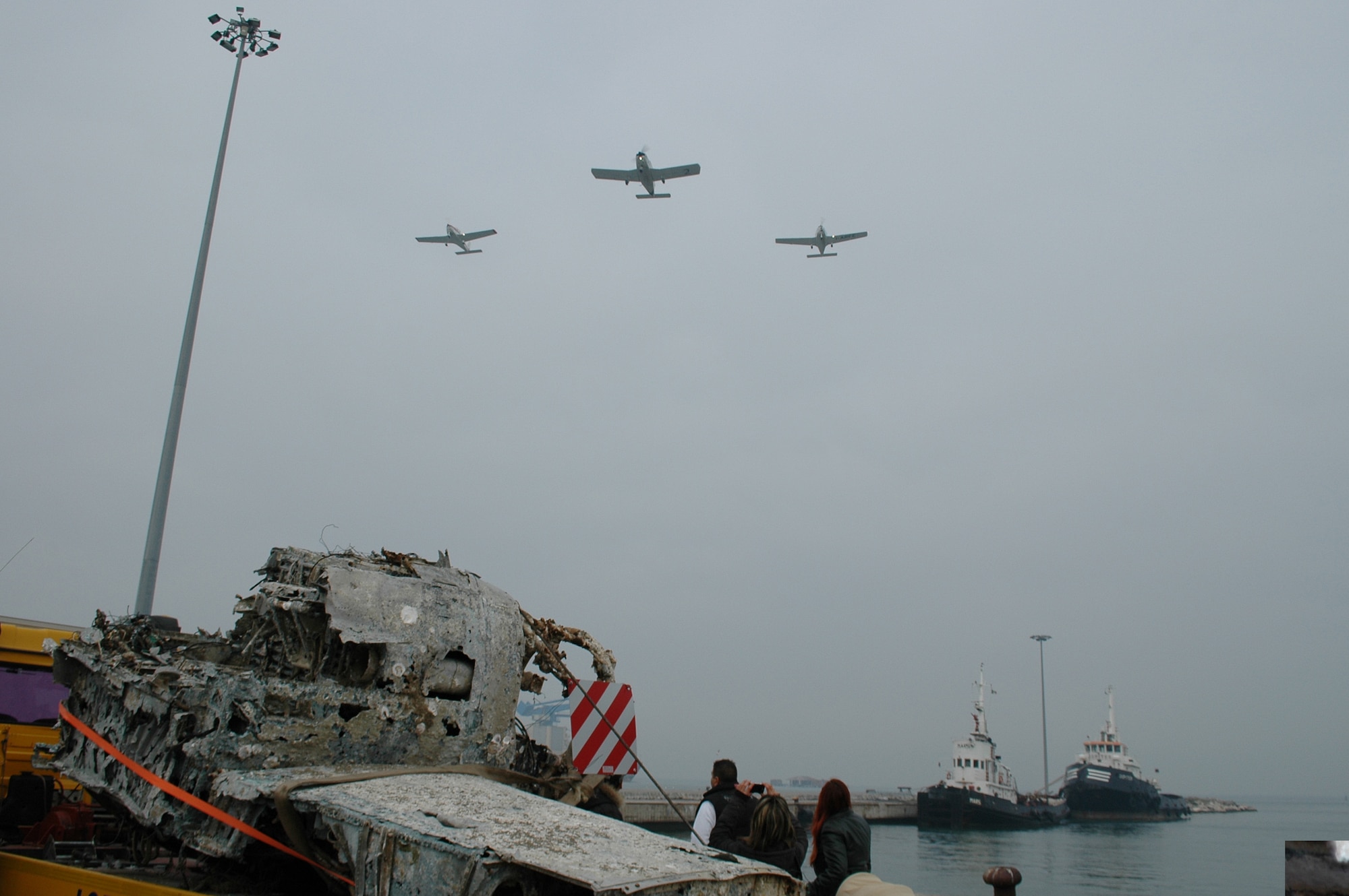 An Italian fisherman and his family look on as an Italian aero club performs a ceremonial fly-over during a ceremony Nov. 14, 2009 in Chioggia, Italy.  The ceremony honored the unknown pilot and other pilots past and present, and transferred the wreckage believed to be that of a P-47 Thunderbolt recovered from the bottom of the Adriatic Sea May 12, 2009, to an Italian aero club who will begin a restoration project expected to take two years.  (U.S. Air Force photo/Tech. Sgt. Michael O'Connor)
