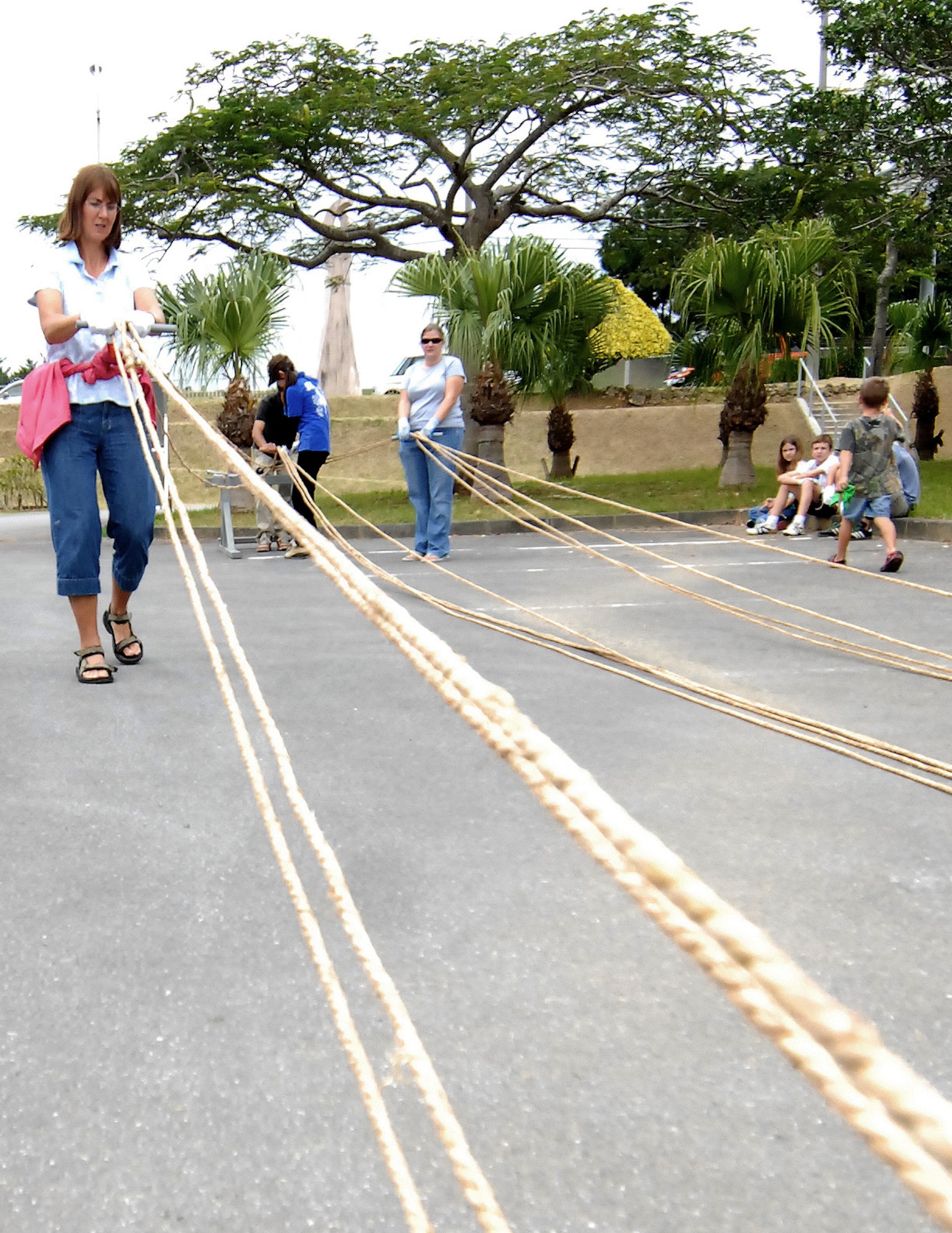 (Left) Lynda Dyer, wife of Navy Cmdr. Lew Dyer at Camp Lester Naval Hospital, helps weave rope for a tug-of-war rope outside Kadena's Gate 5 Nov. 15. Volunteers from Kadena and neighboring installations came together to help Okinawans build a 3-ton, 300-yard long tug-of-war rope that will be used in the Okinawa City International Carnival and Gate 2 Fest Nov. 21. The tug-of-war, which is one of the highlights of the two-day festival, begins at 6 p.m. on Gate 2 Street off base. The carnival right outside Kadena's Gate 2 begins Saturday at 1 p.m. and ends Sunday night at 9 p.m. (Air Force/Staff Sgt. Jason Lake)