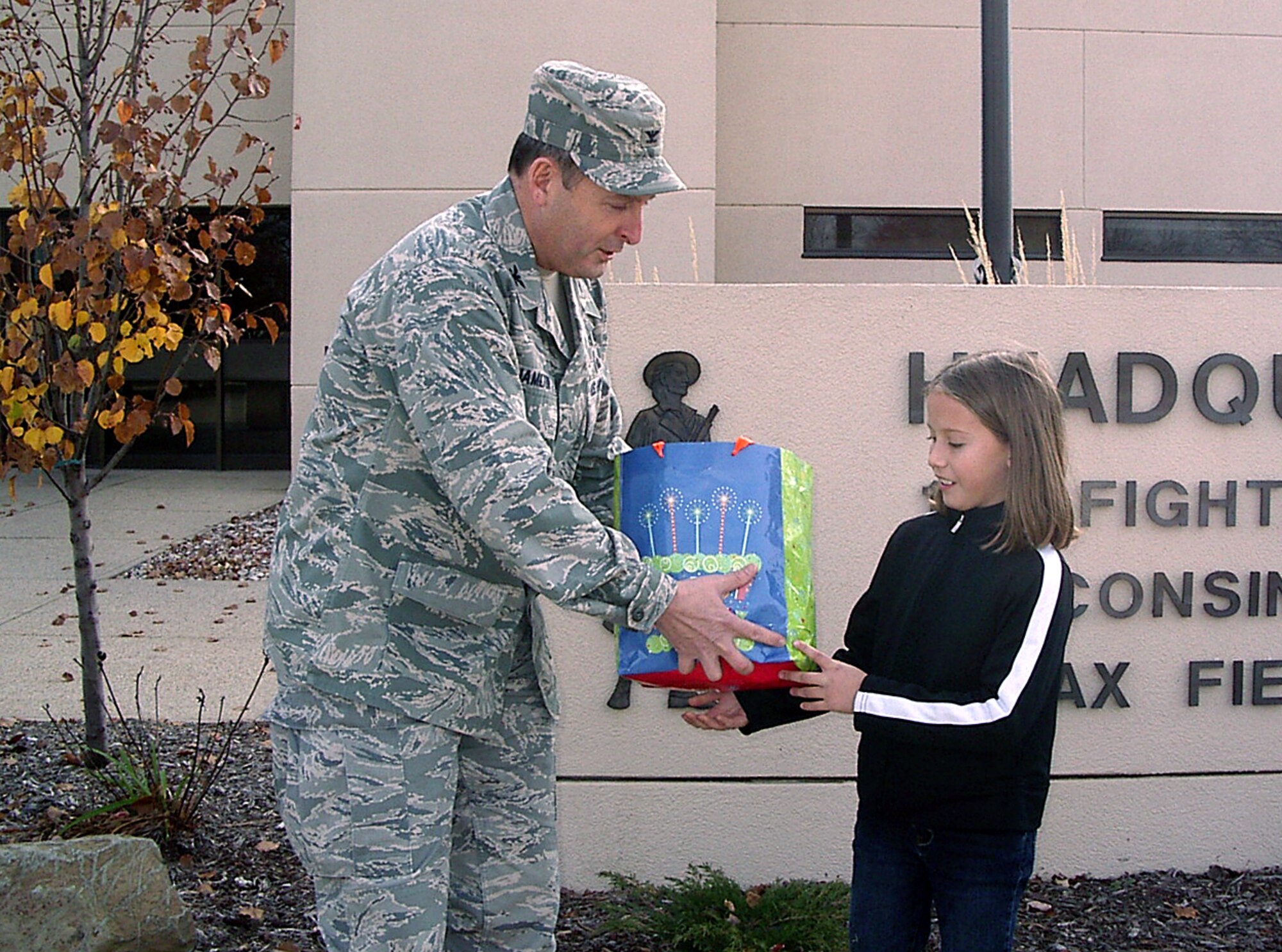 Col. Don Hamilton, Mission Support Group Commander at the 115th Fighter Wing in Madison, Wis., accepts a care package for the troops from Nichollette Volle (ten), daughter of unit member Tech Sgt. Brian Wyman and family readiness volunteer Shawna Wyman Nov. 12, 2009.  The gift was part of a larger donation from Nichollette, who recently asked her birthday party guests to bring items for the troops in lieu of a birthday present for her. The 115th FW family program's Care Packages for Troops volunteers recently assembled over 30 packages to send to unit members who will be deployed over the holidays.  (U.S. Air Force Photo by Master Sgt. Jeff Reese)
