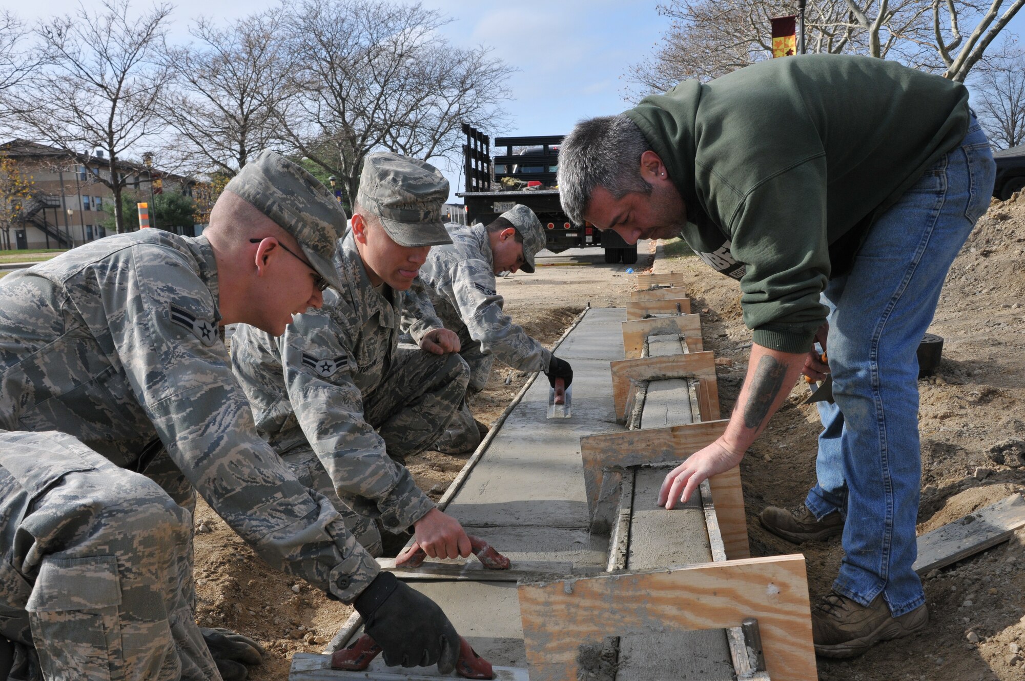 Members of the 87th Civil Engineering Squadron Horizontal Shop, commonly known as the "Dirt Boys" apply the finishing touches to a sidewalk curb on Tuskegee Airman Ave. on McGuire Nov. 18. Michael Mattay, an engineering operator, and Airmen 1st Class Travis Hammer, Rezeq Khalifeh and Steven Stopani designed the wooden form for the curve by hand to meet mission requirements. (U.S. Air Force photo/Pascual Flores)