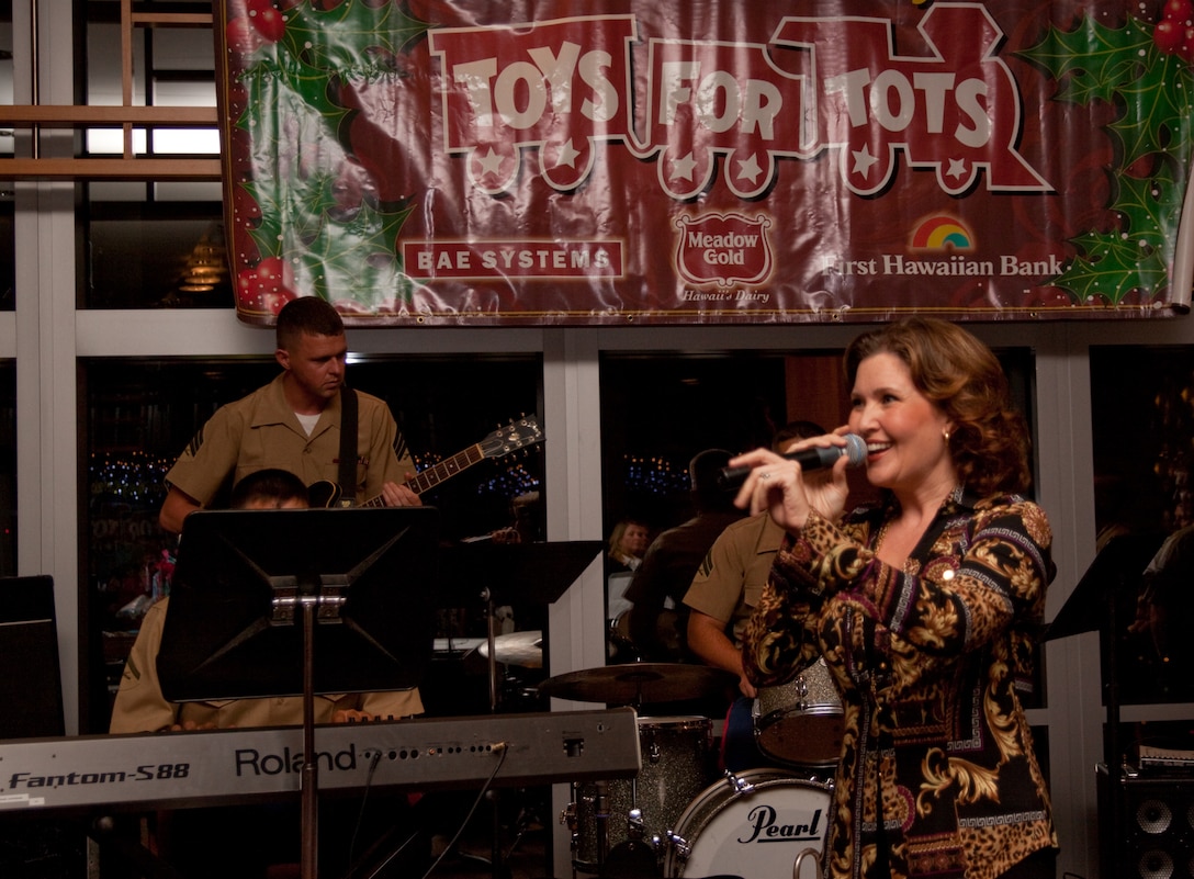 The U.S. Marine Corps Forces, Pacific Band accompanies local entertainer Anita Hall as she sings holiday tunes during a Toys for Tots corporate sponsors’ reception at the First Hawaiian Bank building here Nov. 19. Sponsors were presented with plaques to thank them for their contributions to the Marine Corps Reserve’s Toys for Tots program.