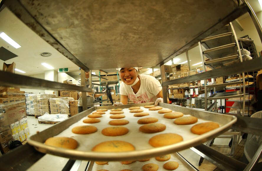 Kanako Nakazato, a Nikkei Business School student, places cookies on a rack to cool Nov. 18. Ms. Nakazato is one of the volunteers preparing cookies for servicemembers living in the dorms at Kadena Air Base. The Hometown Kadena Cookie Drive volunteers prepared more than 24,000 cookies that will be delivered to dorm residents by first sergeants and other representatives Dec. 14. "It's our way of giving them a little taste of home," said Mrs. Sheri Fletcher, one of the event coordinators. (U.S. Air Force photo/Tech. Sgt. Rey Ramon) 
