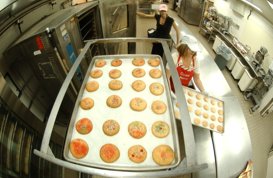 Mrs. Sheri Fletcher and Mrs. Kathy Banks, coordinators for the Hometown Kadena Cookie Drive, remove cookies from the oven Nov. 18. The Hometown Kadena Cookie Drive volunteers prepared more than 24,000 cookies that will be delivered to dorm residents by first sergeants and other representatives Dec. 14. "It's our way of giving them a little taste of home," said Mrs. Fletcher.  (U.S. Air Force photo/Tech. Sgt. Rey Ramon) 

