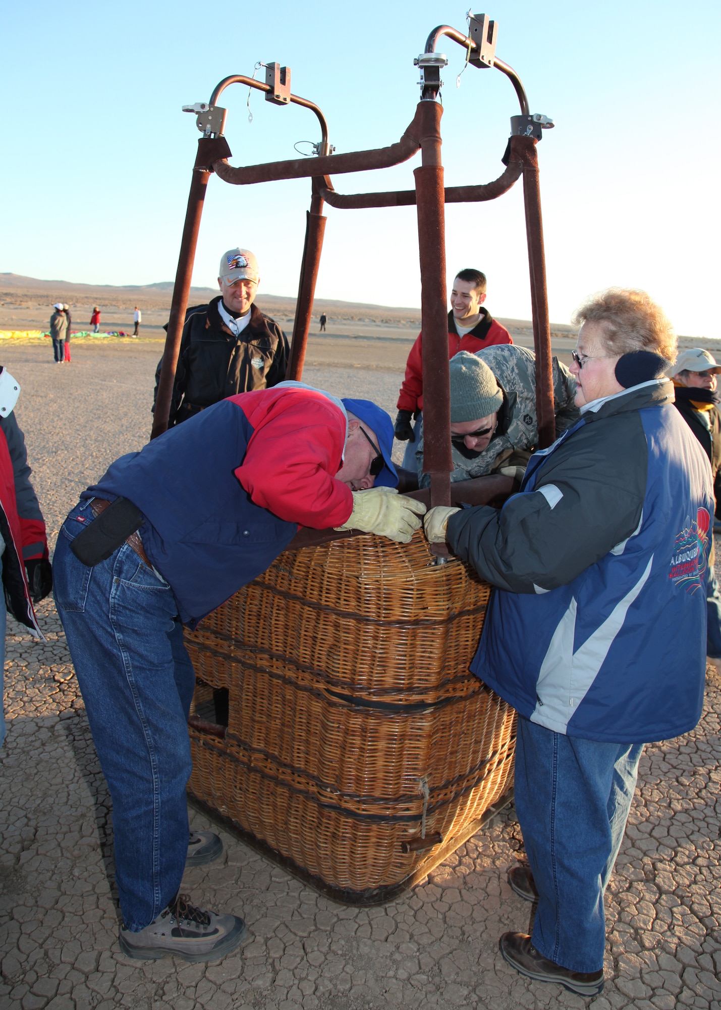 Chief Master Sgt. Mark Brejcha, 412th Test Wing commmand chief, asists hot air balloon crew members as they prepare a basket for launch as Maj. Gen. David Eichhorn, Air Force Flight Test Center commander, looks on at Rosamond Dry Lakebed, Edwards Air Force Base Nov. 15.  Hot air ballooning is a social event that requires leadership skills, team work, and all of the other essentials of aviation. (Air Force photo/ Bobbi Zapka)