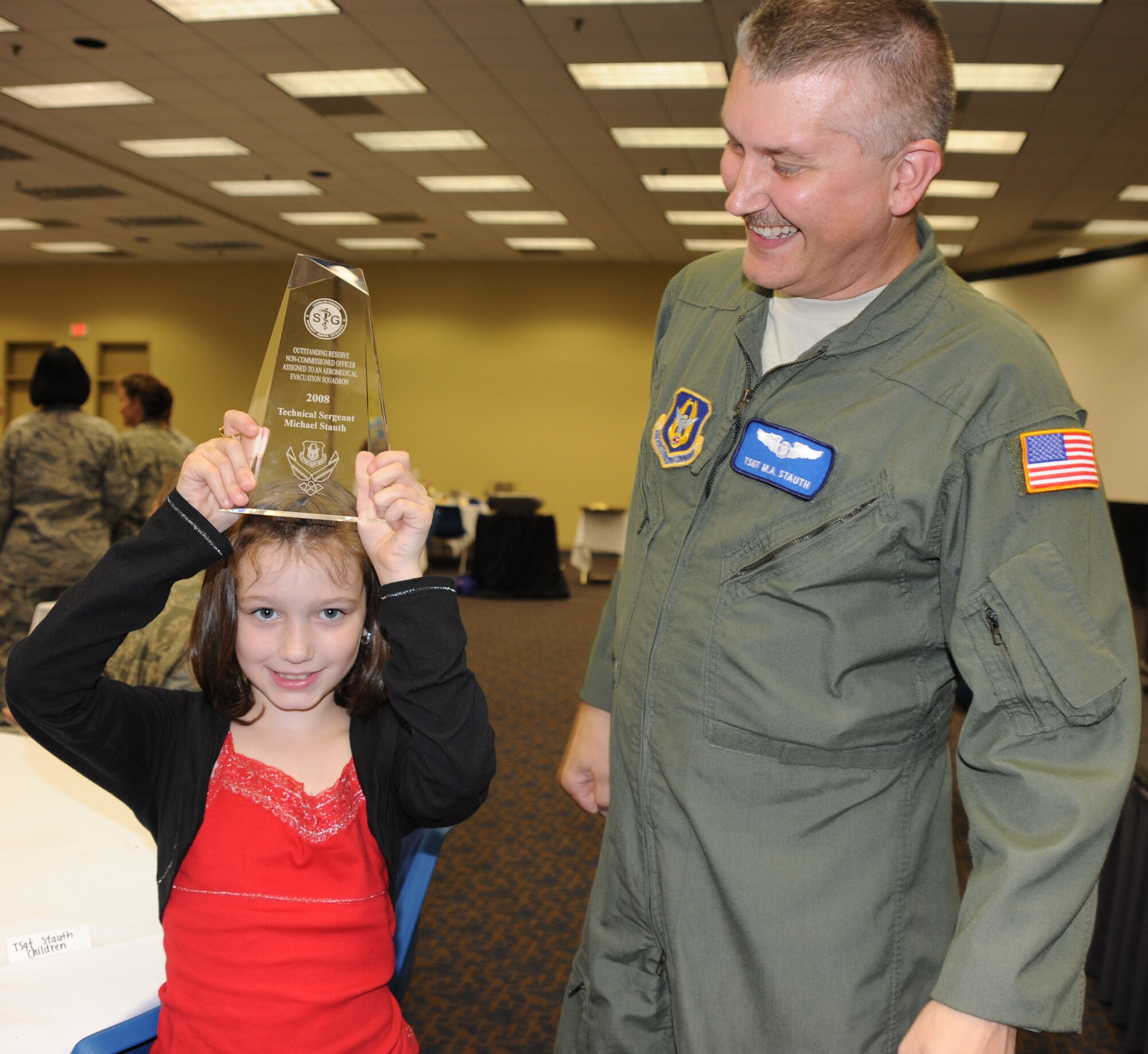Tech. Sgt. Michael Stauth, 932nd Aeromedical Evacuation Squadron, smiles in appreciation as his daughter raises his winning trophy at the AMSUS awards luncheon held in Saint Louis.  He was awarded the etched trophy as the Outstanding Reserve Non-commissioned Officer Assigned to an Aeromedical Evacuation Squadron.  (U.S. photo/Maj. Stan Paregien)