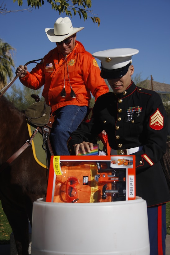 Sgt. Jacobo Hernandez, a Marine volunteer with the Toys for Tots Foundation, puts toys in the donation barrel from the San Bernardino County Sheriff's Department Mounted Search and Rescue rider George Bowman at the base of the Combat Center's flag pole Nov. 22.