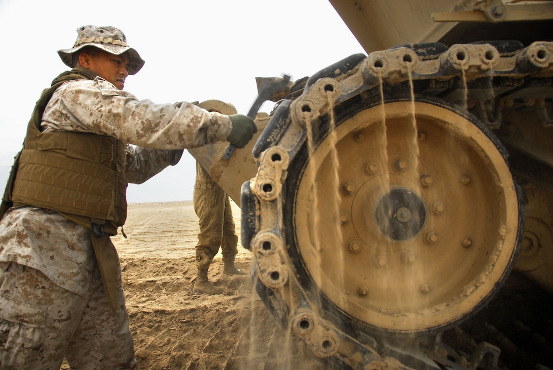 Navy Lt. Ryan Bareng, Battalion Landing Team 2/4 chaplain, helps inspect tracks on an M1A1 Abrams with tankers from the ground combat element’s tank detachment on this uninhabited island Nov. 21. Ground and logistics combat elements of the 11th Marine Expeditionary Unit landed Nov. 20 from the amphibious transport dock ship Cleveland and the amphibious dock landing ship Rushmore.