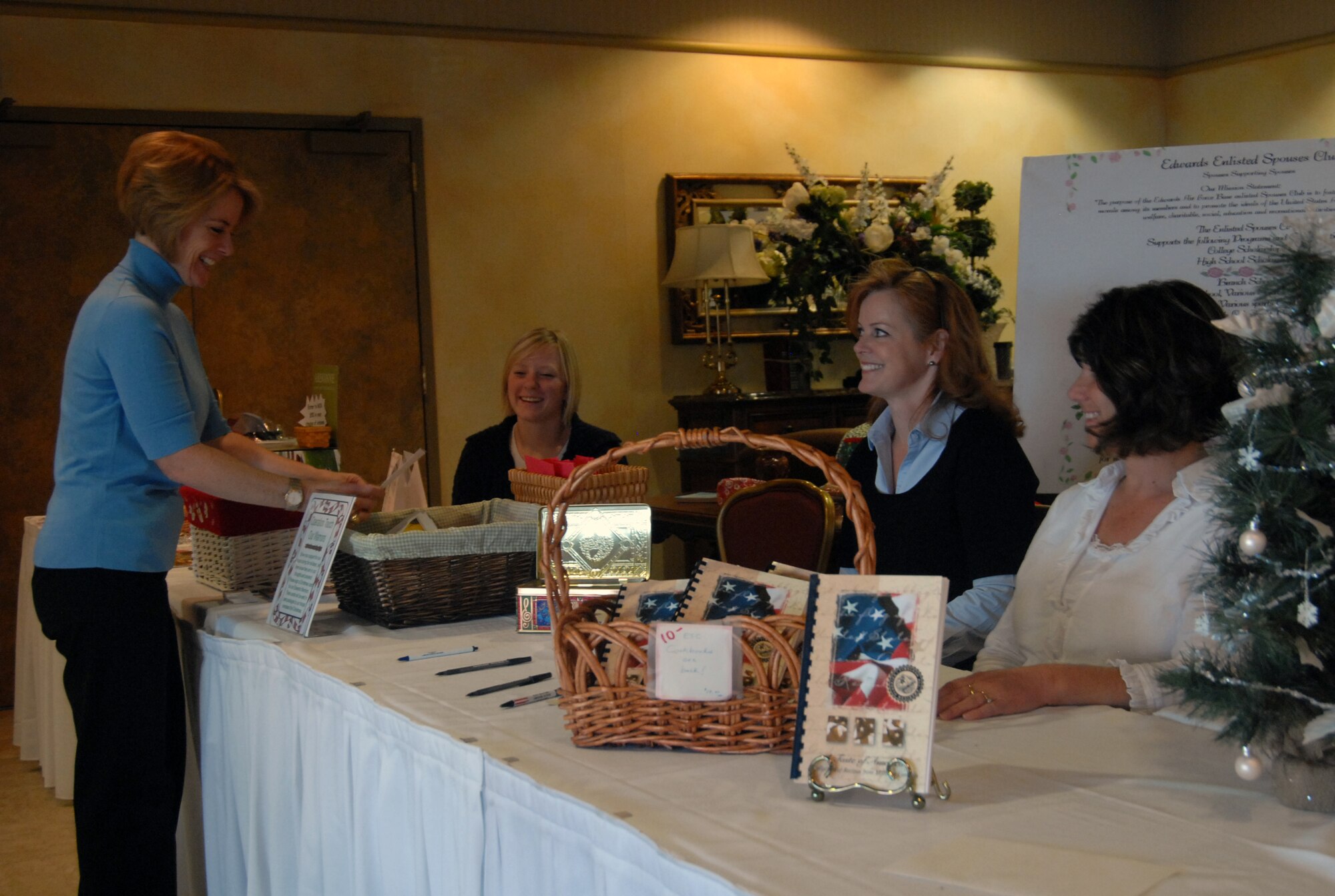 Heather Gubelli enscribes a holiday message in a card Nov. 20 at the annual Mistletoe Bazaar in support of Operation Touch Our Warriors as members of the Edwards Enlisted Spouses Club, Kristen Hurley (left), Laura Jaren (center) and Heather Urban (right) look on. The Edwards Enlisted Spouses Club hosts the Mistletoe Bazaar in order to support community programs. (Air Force photo/ 2nd Lt. Belena Marquez)