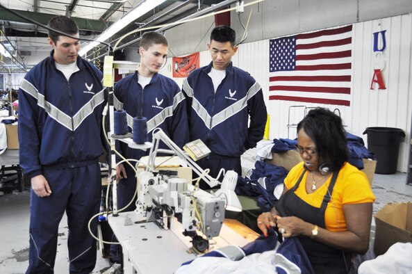 1st Lts. Joseph Castro, Erik Svendsen and Andy Lee wear the Air Force's improved physical training uniform and watch as Angela Smith hems the anti-microbial liner into the new uniform during a tour of the facility Nov. 3, 2009, in Columbus, Miss. The lieutenants are from the 14th Operations Support Squadron at Columbus Air Force Base, Miss. Ms. Smith is an American Power Source seamstress. (U.S. Air Force photo/Sonic Johnson)