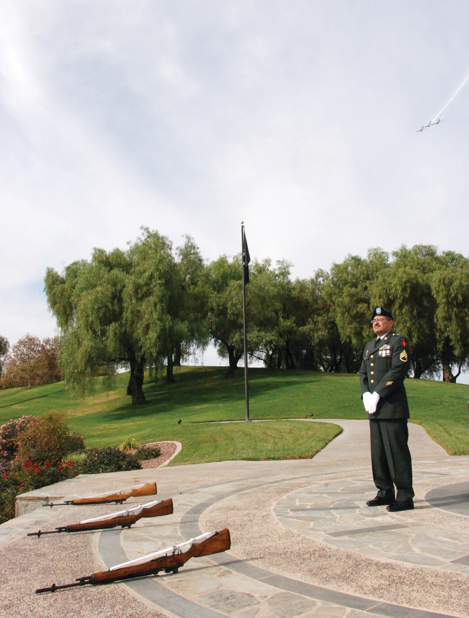 A trio of planes fly overhead while Army Staff Sgt. Arthur Ledesma, Jr., stands watch over the color guard rifles. Sergeant Ledesma is a member of the 491st Military Police Company and is in training with the Blue Eagles Total Force Honor Guard.(U.S. Air Force photos by Megan Just)