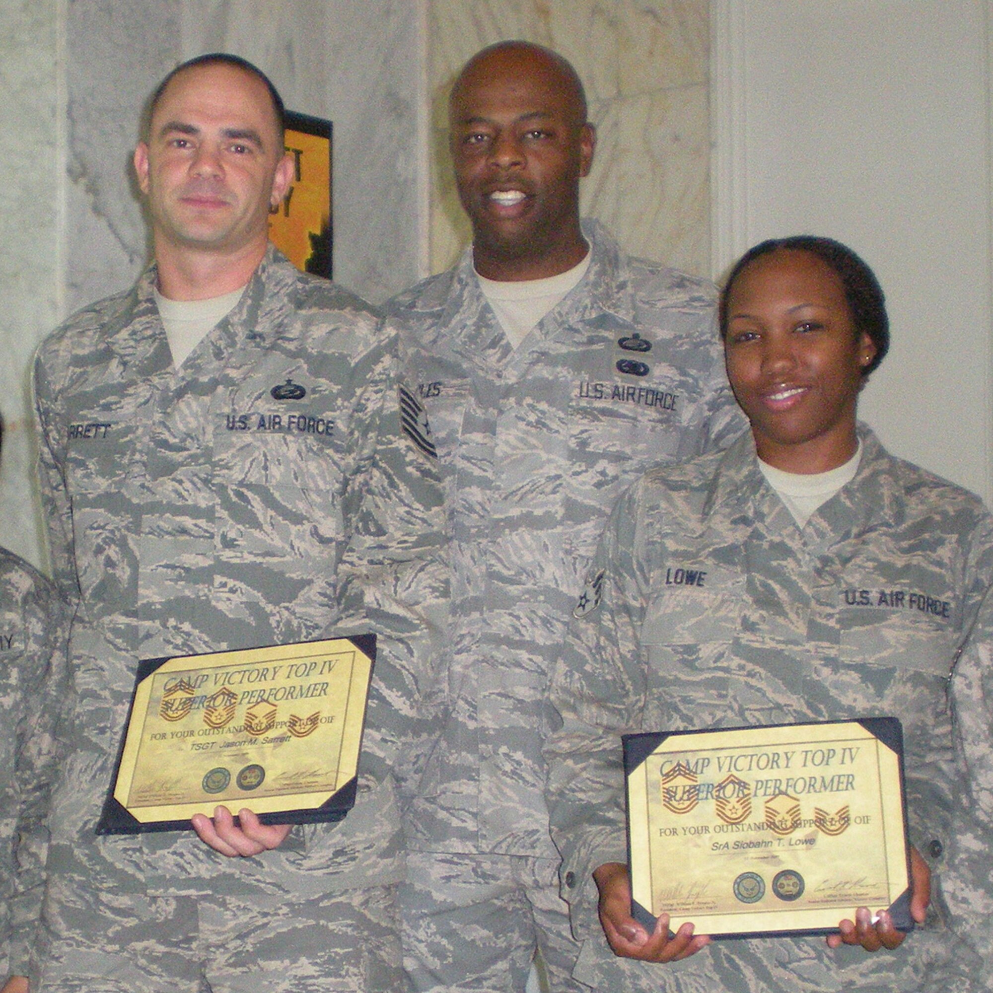 VICTORY BASE COMPLEX, Baghdad – Tech. Sgt. Jason Sarrett (left) and  Senior 
Airman Siobahn Lowe (right) receive letters of appreciation and a Top IV coin from Senior Master Sgt. William Peoples, Victory Base Complex Top IV president.  Both individuals were recognized for sustained superior performance and their contributions to Operation Iraqi Freedom. Tech. Sgt. Sarrett is the noncommissioned officer in charge of plans and operations for Multinational Corps-Iraq, CJ1. He is deployed from Eglin Air Force Base, Fla. and hails from San Antonio, Texas. Airman Lowe is a coalition awards clerk for MNC-I, C1, deployed from Goodfellow AFB,Texas, and is a native of Fayetteville, N.C. (Courtesy photo)