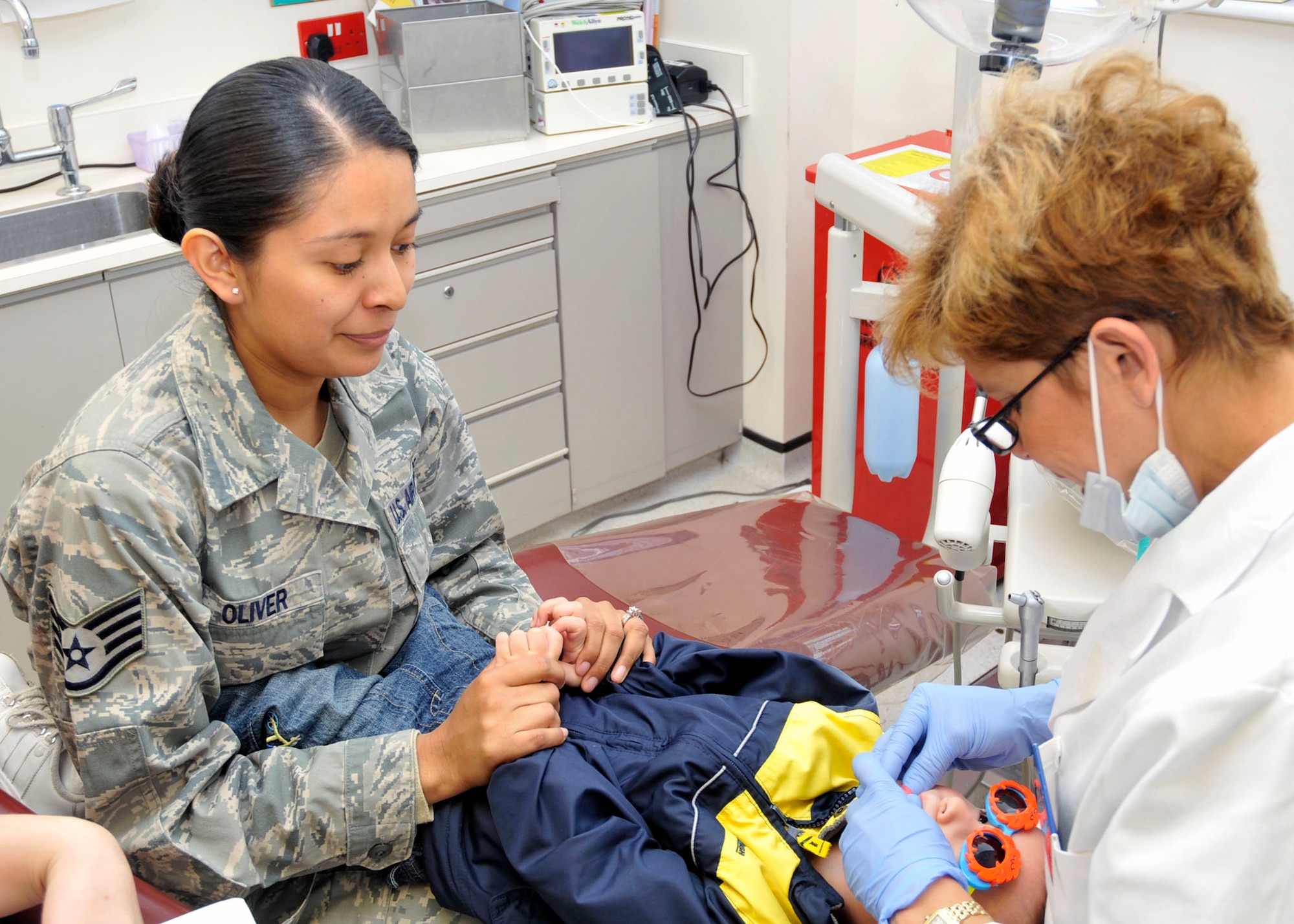 Royal Air Force Lakenheath, England -- Staff Sgt. Maria Oliver, 48th Medical Operations Squadron ultrasound technician, holds her son’s hands, Brock, age 2, as Lt. Col. Aixa Torres-Ramirez, 48th Dental Squadron pediatric dentistry officer in charge, administrates a dental exam at RAF Lakenheath, England, Oct. 14.  The proper care of children’s teeth is an important part of their oral health and should be accomplished routinely.  (U.S. Air Force photo/ Airman 1st Class Eboni Knox) 