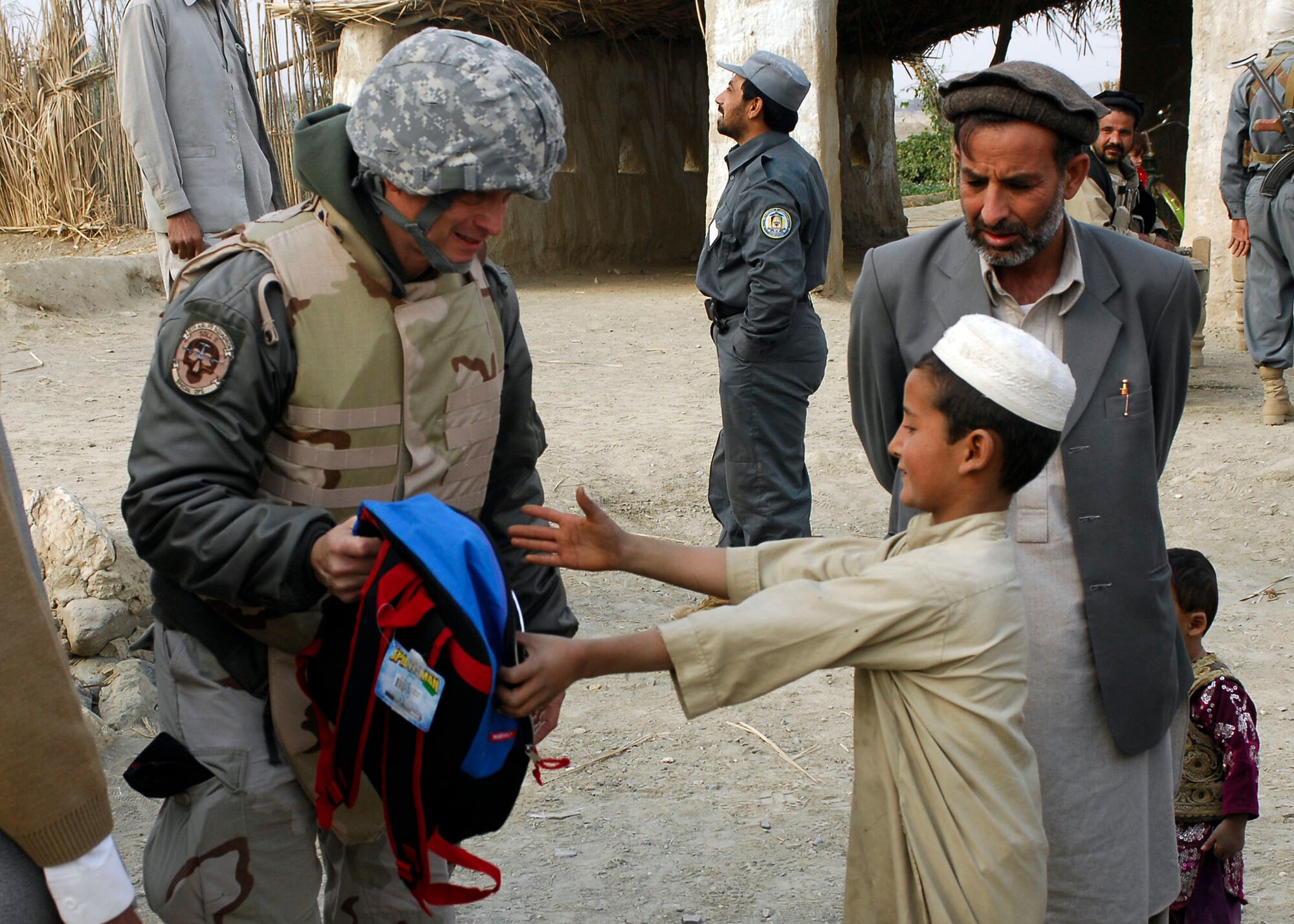 BAGRAM AIRFIELD, Afghanistan -- Gary Sinise (left) hands a back pack to an Afghan child Nov. 23, 2009.  Mr. Sinise stopped at the school, on his way to Forward Operating Base Goshta, to hand out back packs full of school supplies, shoes and other necessities to local children.  (U.S. Air Force photo/Senior Airman Felicia Juenke)