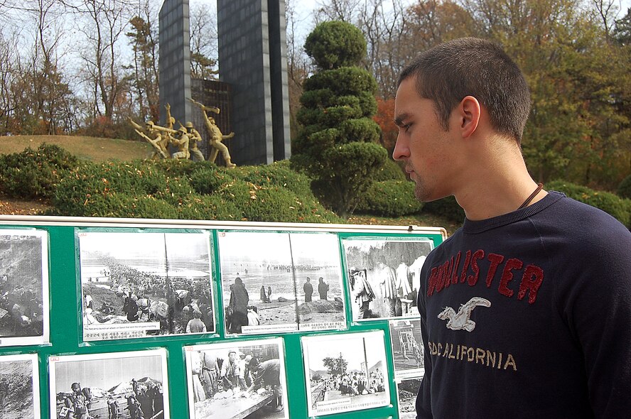 Airman 1st Class Todd Scarbrough from Kunsan Air Base, South Korea,  looks at photos from the Korean War on display Nov. 12  in front of a monument honoring Task Force Smith in the UN Forces' first battle during the war. He was part of a friendship tour group who held a wreath laying ceremony at the monument in Osan. (U.S. Air Force photo by Staff Sgt. Beth Del Vecchio)