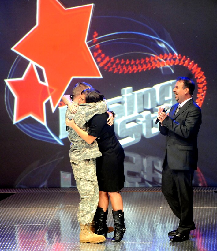 U.S. Army Capt. Donald Williamson, a chaplain at the U.S. Army Garrison in Bamberg, Germany, gives 2009 Operation Rising Star winner Lisa Pratt of Fort Carson, Colo., a congratulatory hug in front of co-host Victor Hurtado at Wallace Theater on  Fort Belvoir, Va., Nov. 20, 2009.