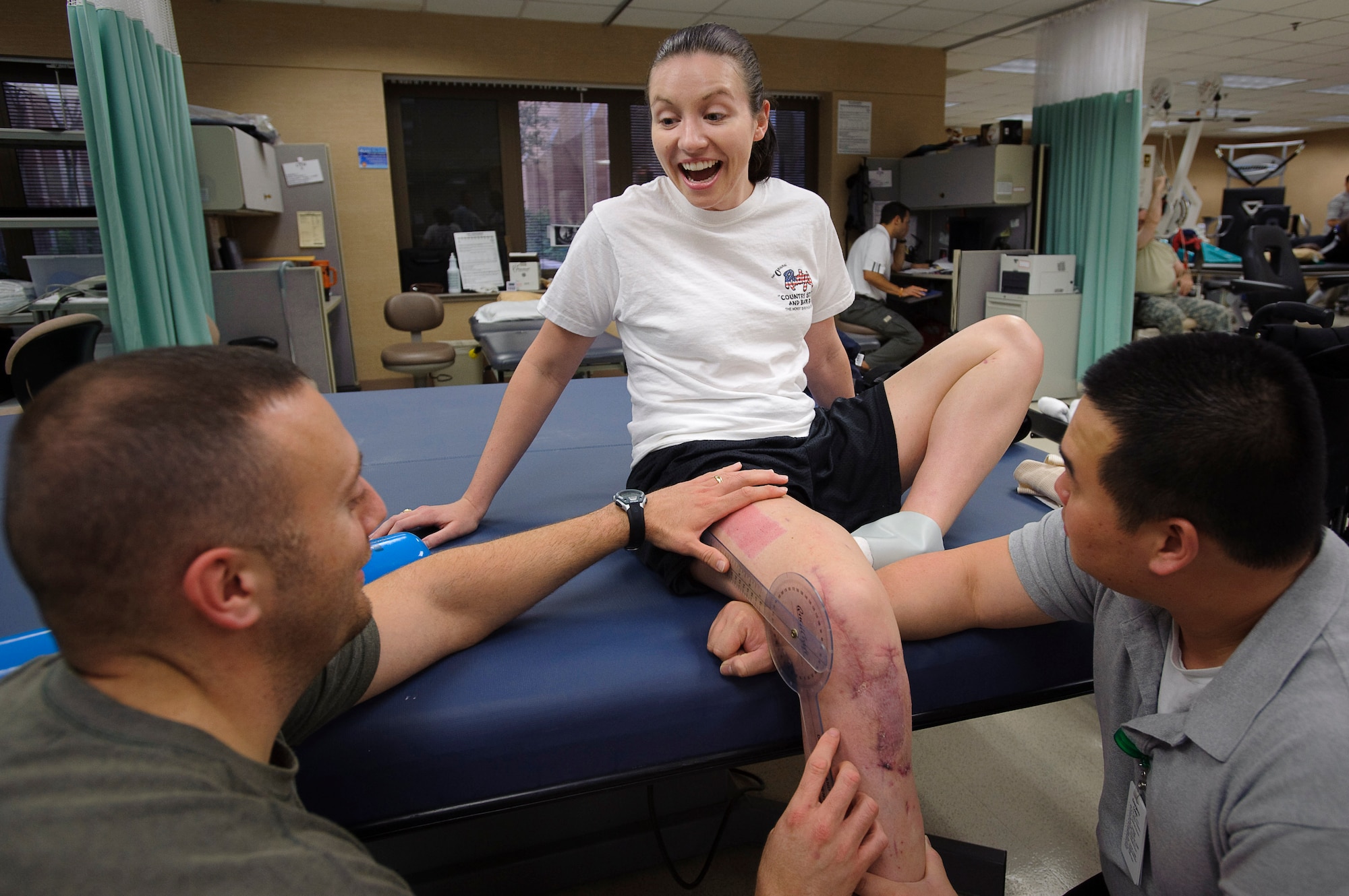 Capt. wendy Kosek (c) 19th Airlift Wing legal officer, Little Rock Air Force Base, TX, reacts to her latest range of motion test conducted by John Inzinna (l) and Anhtuan Pham physical therapy assistants with Book Army Medical Center?s outpatient physical therapy clinic. When she started physical therapy Kosek had just 30 degrees of mobility in her knee and is currently up to 63, her goal is a 10 degree increase per week. (U.S. Air Force photo/Steve Thurow)