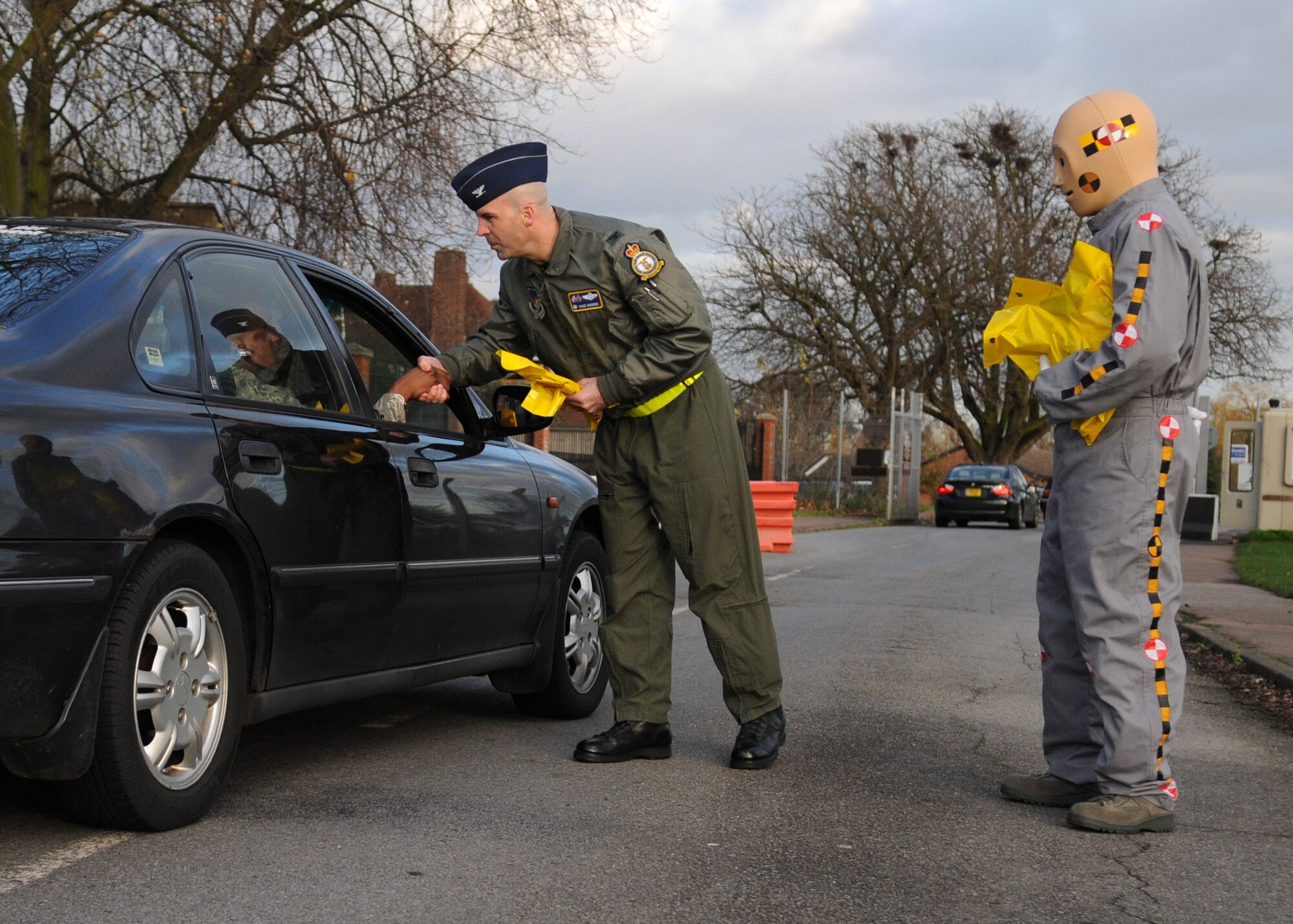 RAF MILDENHALL, England -- Col. Chad Manske, 100th Air Refueling Wing commander, and Vince the crash test dummy provide "Be Safe" reminders and ensure drivers and passengers are wearing seatbelts before leaving base at Gate 1 Nov. 25. Commanders from across the 100th ARW manned base departure gates as Airmen left for the Thanksgiving holiday weekend. A similar event was held earlier this year for Labor Day and contributed to zero driving under the influence citations or vehicle mishaps. (U.S. Air Force photo/Staff Sgt. Jerry Fleshman)
