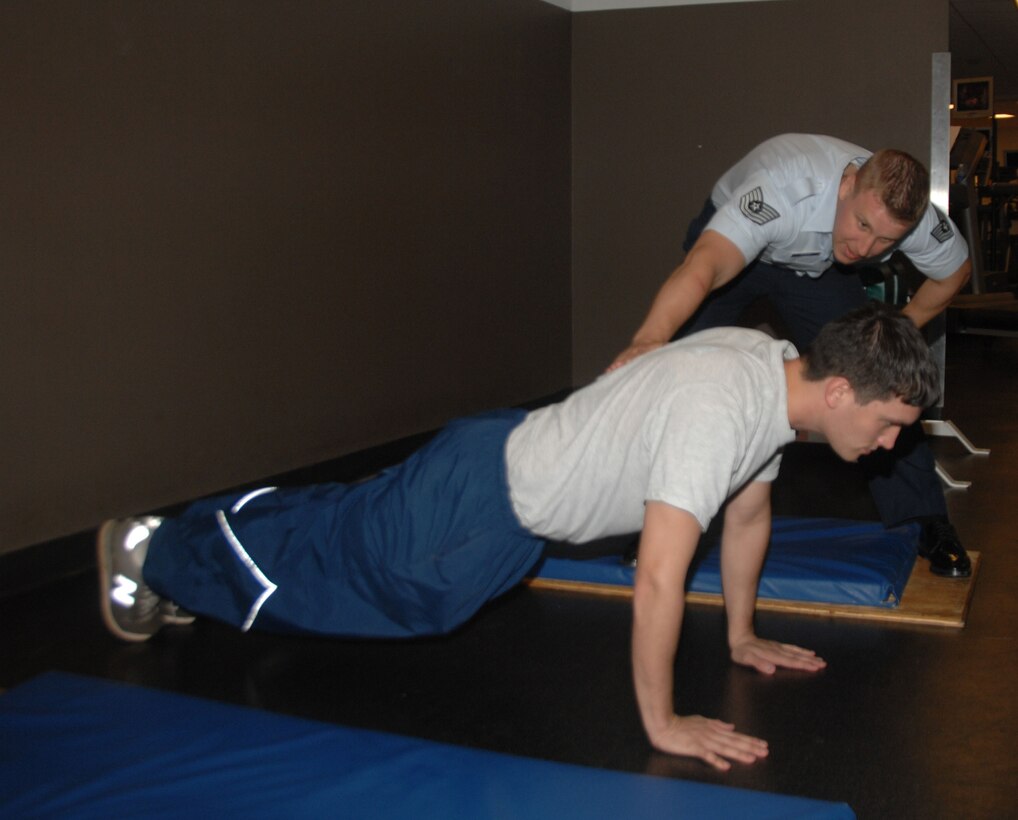 ANDERSEN AIR FORCE BASE, Guam - (Right) Tech. Sgt. Jason Herman, nutrition program manager for the health and wellness center, ensures Senior Airman Jonathan Ardis, 36th Force Support Squadron fitness specialist, keeps his back straight in the "up" position of a push-up here Nov. 30. Correct push-up form is one of many focus areas on the new physical training standards that will be implemented throughout the Air Force July 1. (U.S. Air Force photo by Senior Airman Shane Dunaway)