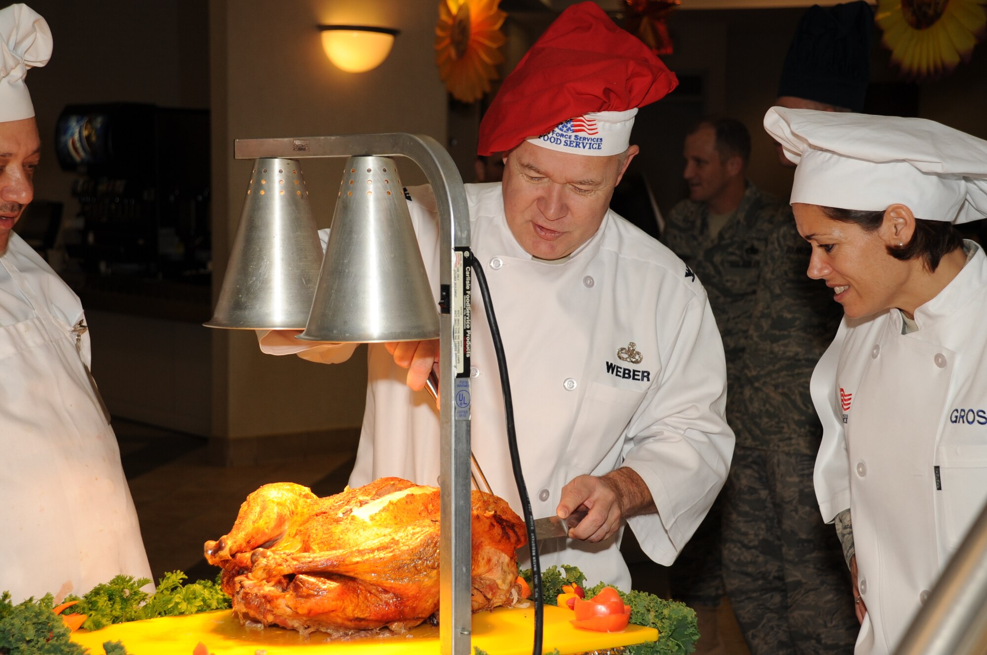 Col. James Weber, 305th Maintenance Group commander, demonstrates his carving skills to Col.Gina Grosso, Joint Base McGuire-Dix-Lakehurst commander, during the Thanksgiving dinner held at  Halverson Dining Facility here Nov. 26. Base leadership served dinner to the troops remaining on base during the holiday (U.S. Air Force photo/Angel Lopez).
