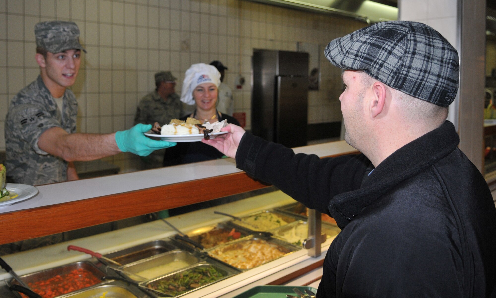 SPANGDAHLEM AIR BASE, Germany -- Airman 1st Class Jeremy Monts, 52nd Force Support Squadron, gives a Thanksgiving plate to Senior Master Sgt. Earle Babb, 52nd Aircraft Maintenance Squadron, as Mara Wight, wife of Col. Tip Wight, 52nd Fighter Wing commander, looks on Nov. 26. Members of the 52nd FW leadership and several other volunteers hosted this year's Thanksgiving meal at the Mosel Dining Facility. (U.S. Air Force photo/Airman 1st Class Nick Wilson)