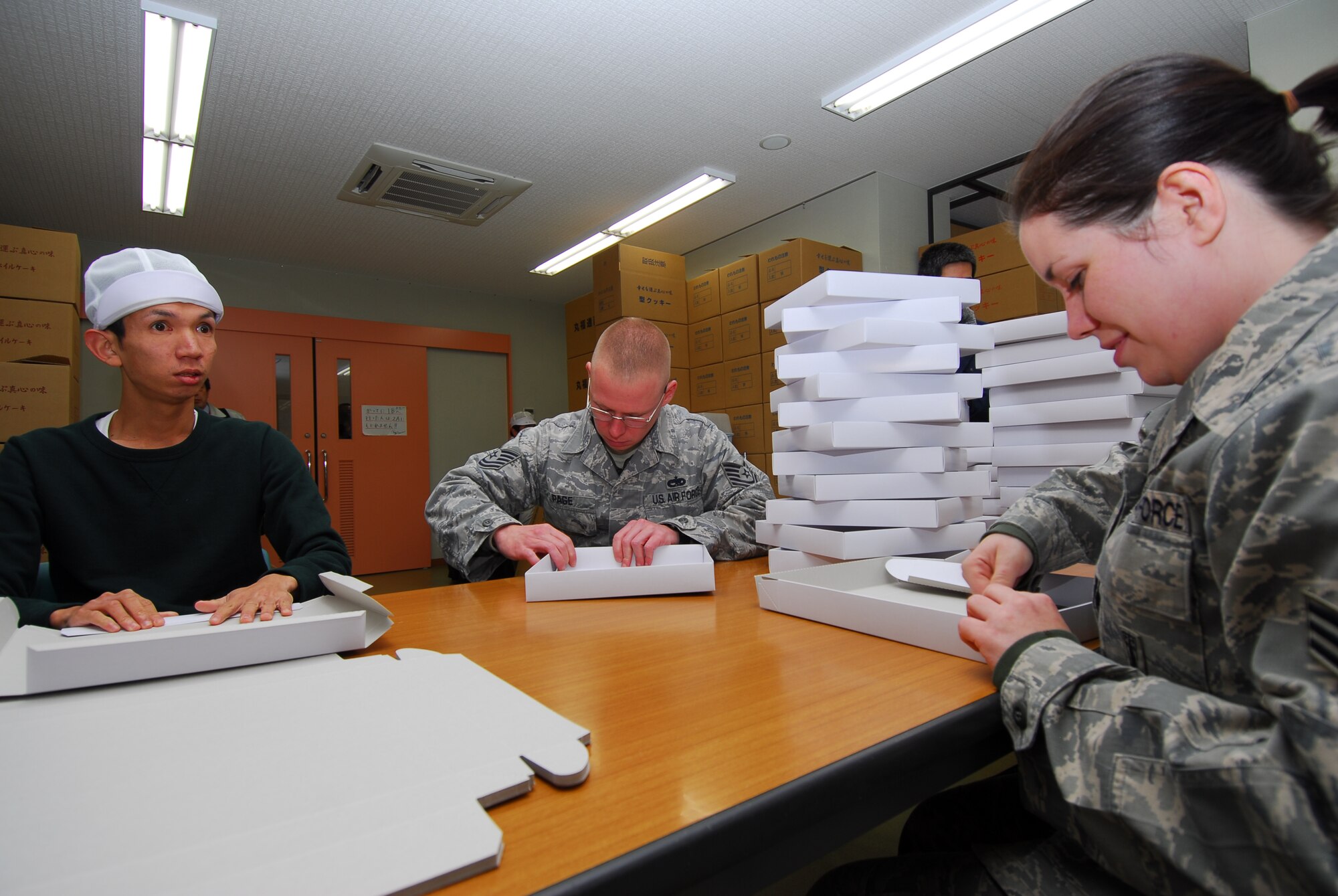 KOMATSU AIR BASE, Japan— Kohei Morimoto, Umenoki Gakuen student, demonstrates proper candy box folding technique to Tech. Sgt. Jeremy Page, 13th Aircraft Maintenance Unit crew chief and Senior Airman Heidi Kiefer, 13th AMU weapons specialist, Nov. 19, at a Komatsu, Japan, welfare center. Umenoki Gakuen School is a job training center developed to give special needs people productive skills. (U.S. Air Force photo/Staff Sgt. Phillip Butterfield)