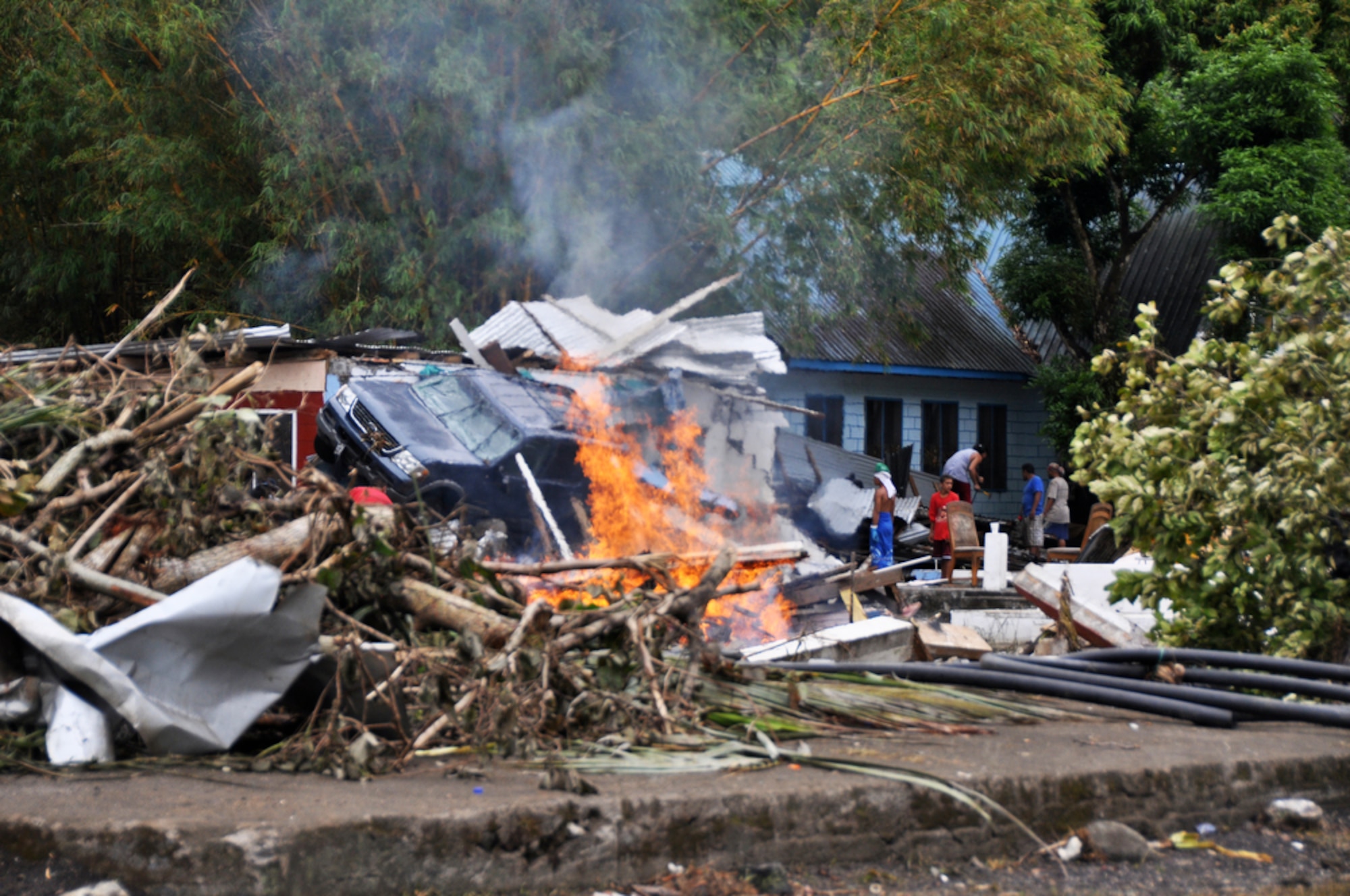 A trash fire buns in the foreground of a car that hangs off the side of porch roof Oct. 1, 2009, in Pago Pago, American Samoa. The island nation was struck Sept. 29 by an 8.3 magnitude earthquake generating 15-foot waves and destroying whole villages. (U.S. Air Force photo/Tech. Sgt. Cohen A. Young) 
