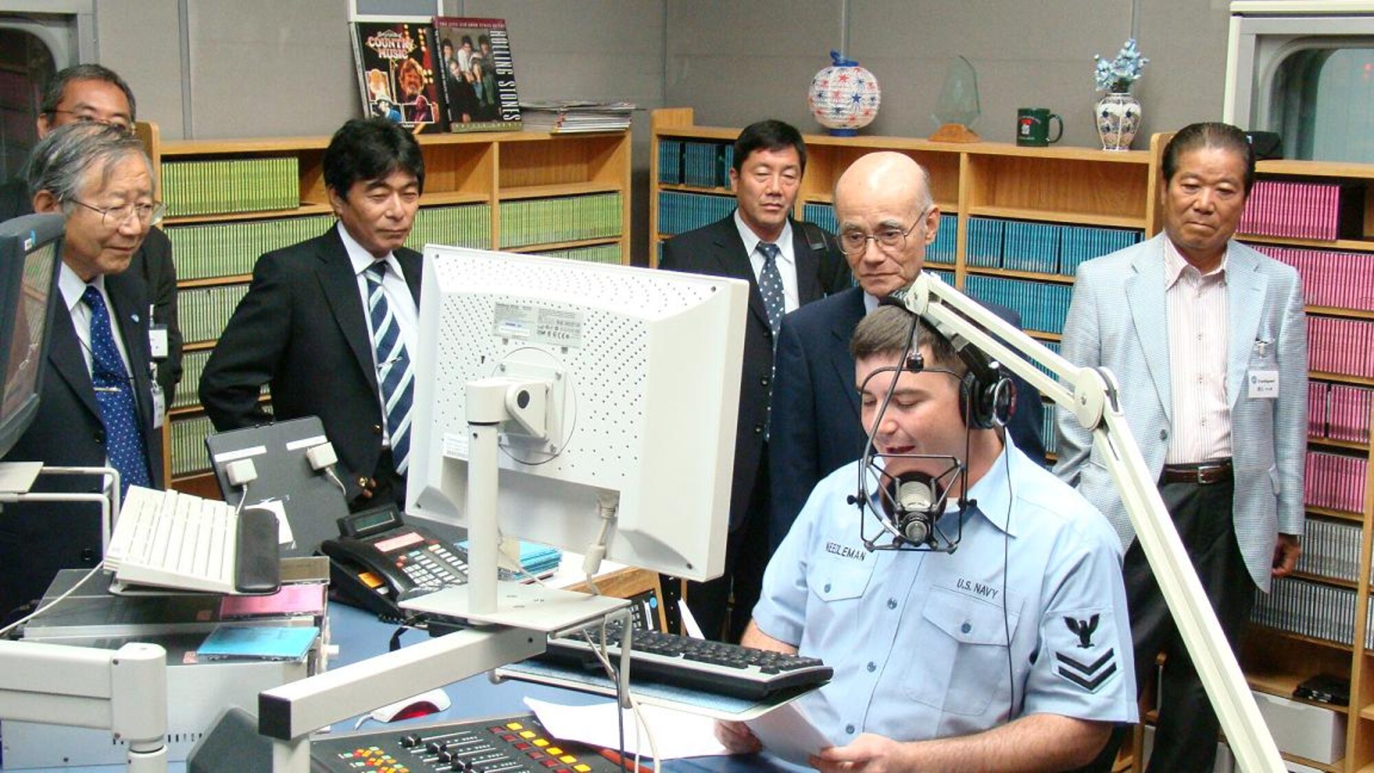 Mass Communications Specialist 2nd Class Isaac Needleman, also known as 'DJ Awesome' on AFN, reads a news report Sept. 30 while members from the Japan-America Air Force Goodwill Association watch.  Since the group’s inception in 1996, JAAGA has become one of the key organizations that supports the bilateral relationship between the U.S. Air Force and the Japan Air Self-Defense Force.  (U.S. Air Force photo by Capt. Will Powell)   