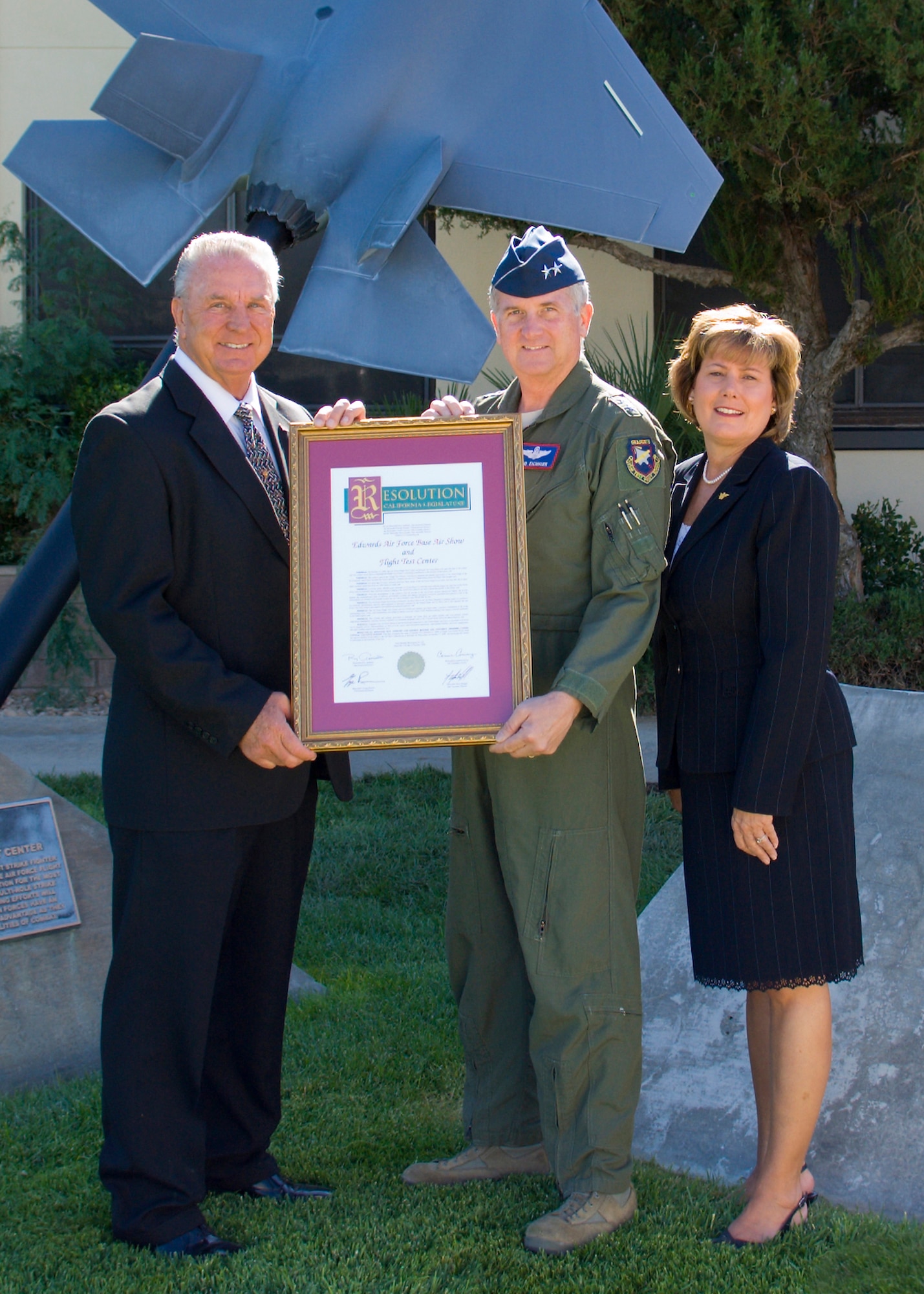 Rex Moen (left) District Representative for Senator Roy Ashburn and Lisa Moulton (right), District Director for Senator George Runner, present a legislative resolution to Maj. Gen. David Eichhorn (middle), Air Force Flight Test Center commander, naming the week of Oct 10 – 17 as Flight Test Nation week. The resolution commemorates Edwards for its historic contribution to aerospace research, progress and development, and also officially recognizes its Flight Test Nation brand prior to the Oct 17 air show and open house at Edwards. (Air Force photo/Mike Cassidy) 
