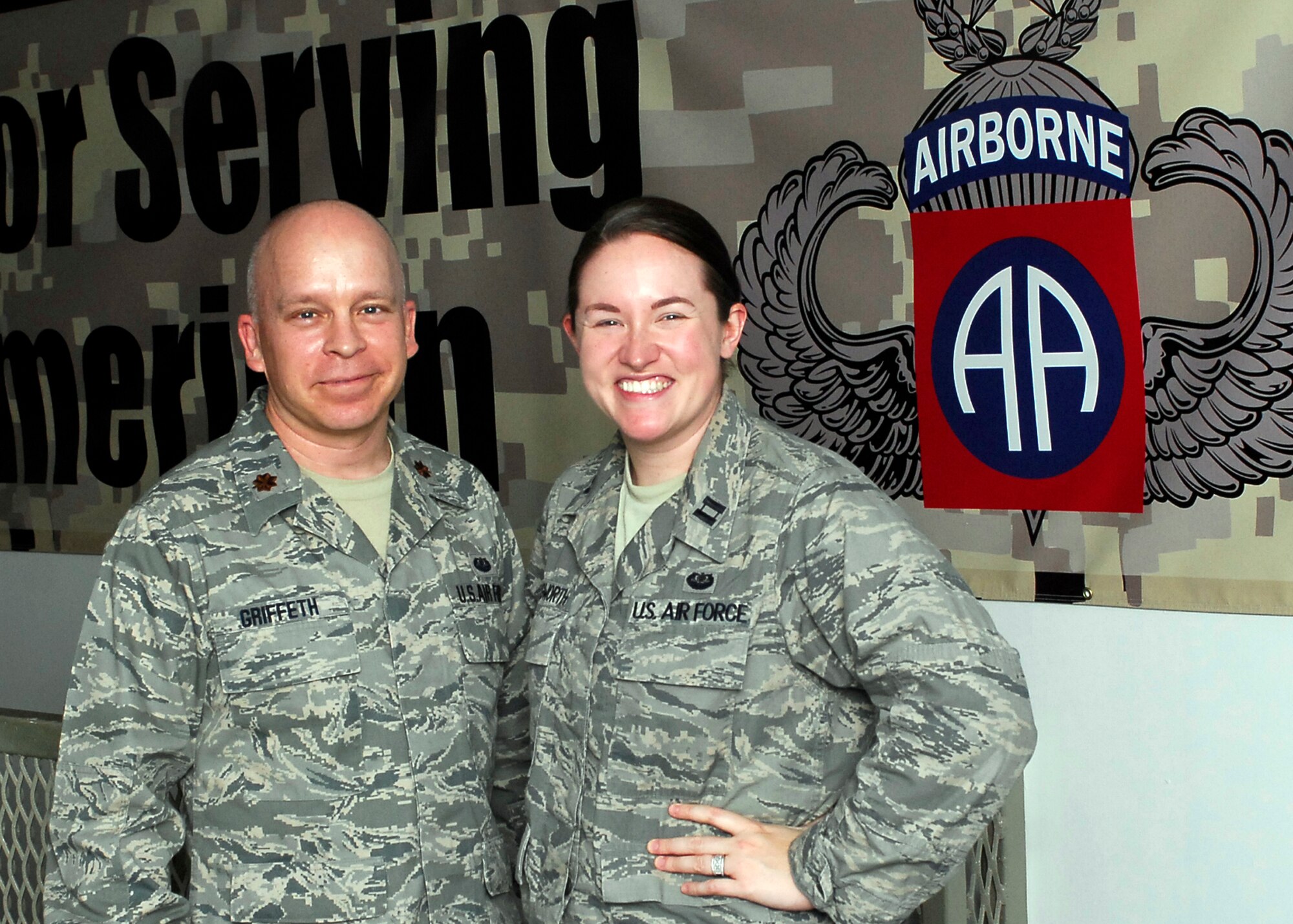 BAGRAM AIRFIELD, Afghanistan -- Major Tobin Griffeth and Capt. Katie Illingworth, Contract and Fiscal lawyers with Combined Joint Task Force 82's Office of the Staff Judge Advocate stand together in front of an 82nd Airborne banner.  The banner reads: "Thank you for serving.  Stay all American." Major Griffeth and Captain Illingworth created a game that would harness the energy of fan support for the University's of Texas and Oklahoma's heated rivalry.  Donations of clothes, shoes and school supplies are sent in to the duo where the help distribute it country-wide to ground patrols to help the Afghan people.  "This war will be one person at a time, and through the children," Major Griffeth said.  (U.S. Air Force/Senior Airman Felicia Juenke)