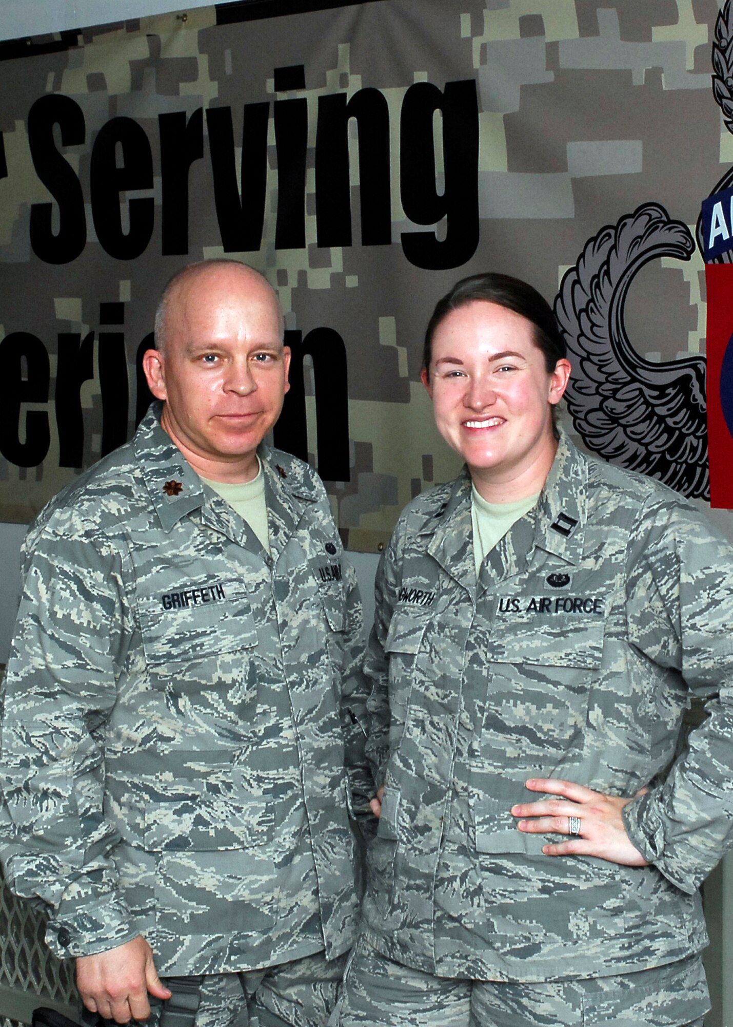 BAGRAM AIRFIELD, Afghanistan -- Major Tobin Griffeth and Capt. Katie Illingworth, Contract and Fiscal lawyers with Combined Joint Task Force 82's Office of the Staff Judge Advocate stand together in front of an 82nd Airborne banner.  The banner reads: "Thank you for serving.  Stay all American." Major Griffeth and Captain Illingworth created a game that would harness the energy of fan support for the University's of Texas and Oklahoma's heated rivalry.  Donations of clothes, shoes and school supplies are sent in to the duo where the help distribute it country-wide to ground patrols to help the Afghan people.  "This war will be one person at a time, and through the children," Major Griffeth said.  (U.S. Air Force/Senior Airman Felicia Juenke)